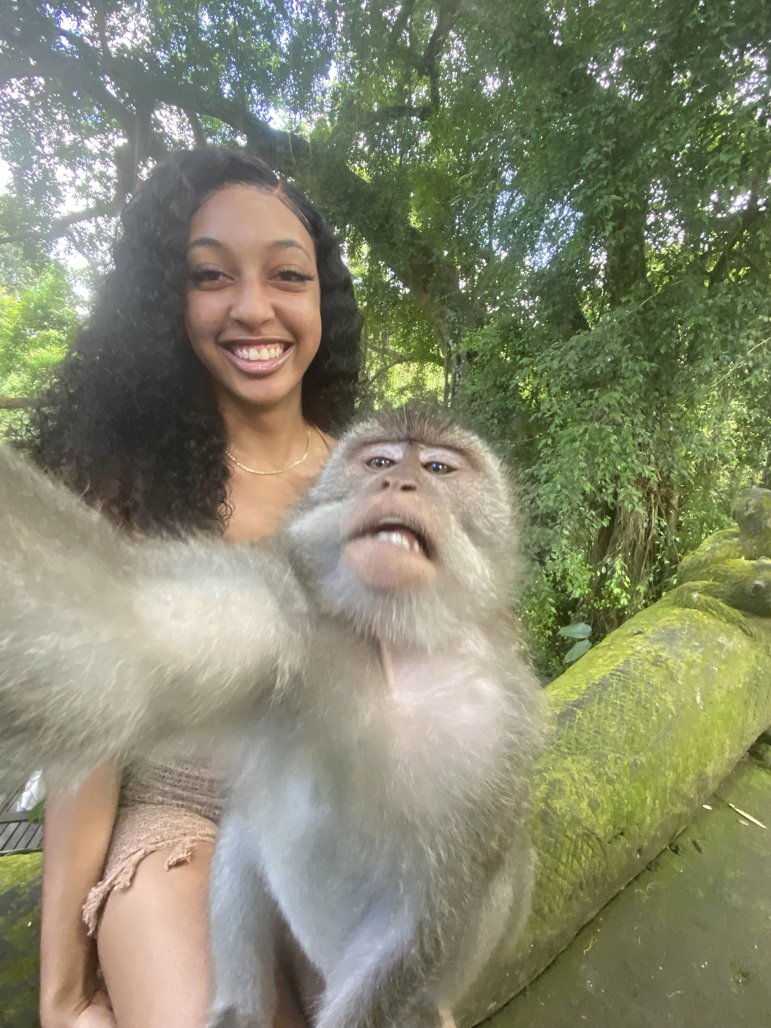 A young woman taking a selfie with a monkey in a lush, green outdoor setting.