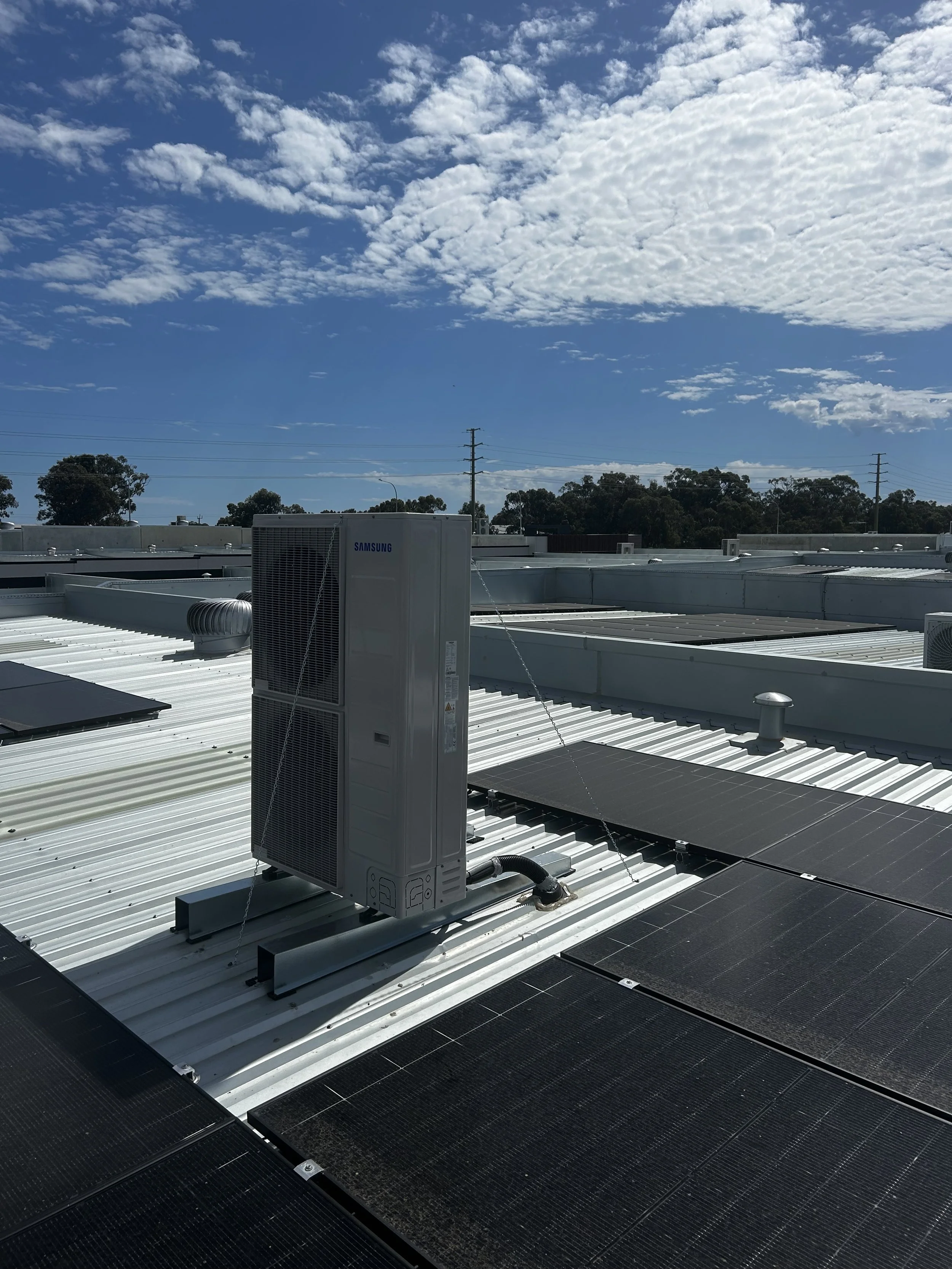 Rooftop with solar panels and HVAC system under a partly cloudy sky.