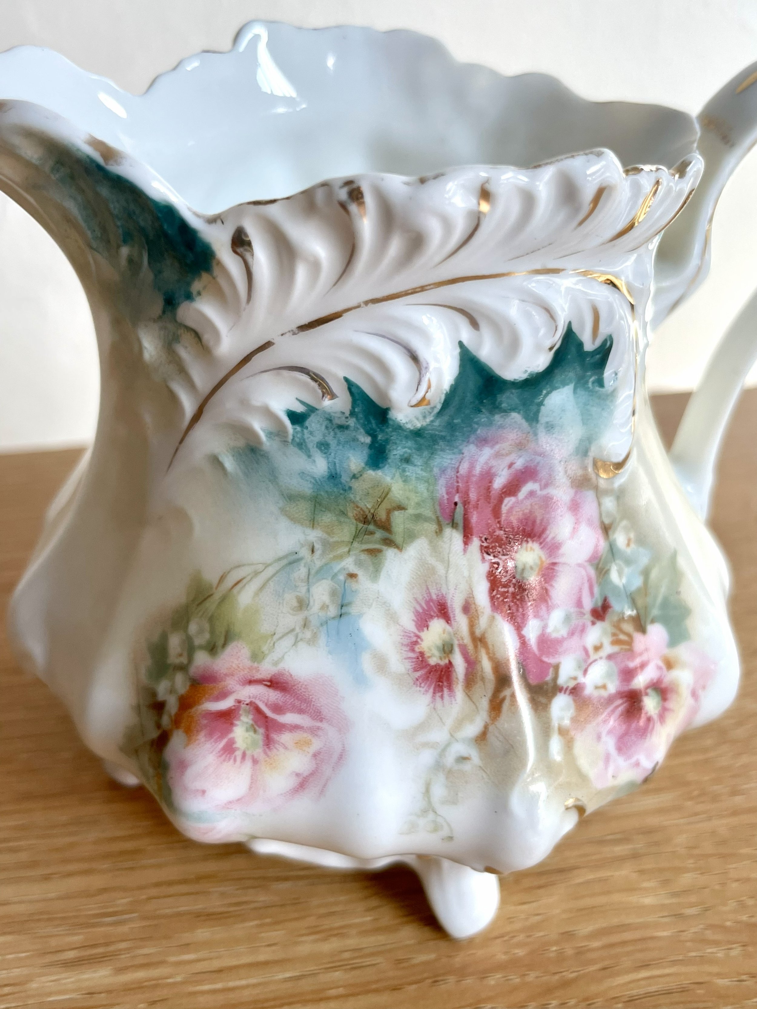 Close-up of a decorative porcelain creamer with floral and leaf pattern, gold accents, and a scalloped rim.