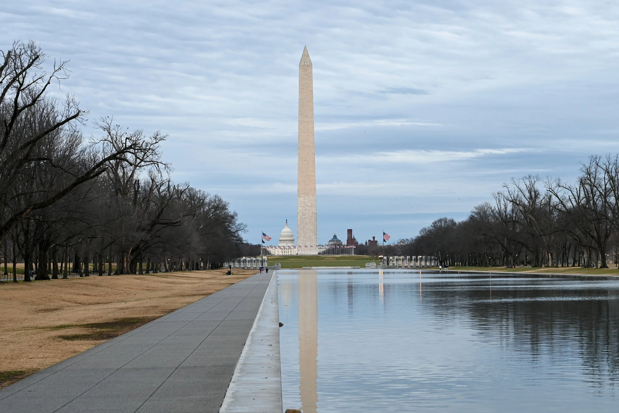Washington Monument with US Capitol and flags in background, reflection in Reflecting Pool.