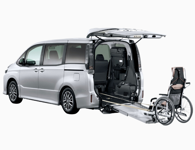 Silver minivan with rear hatch open, wheelchair accessible ramp extended, parked inside a plain white background.