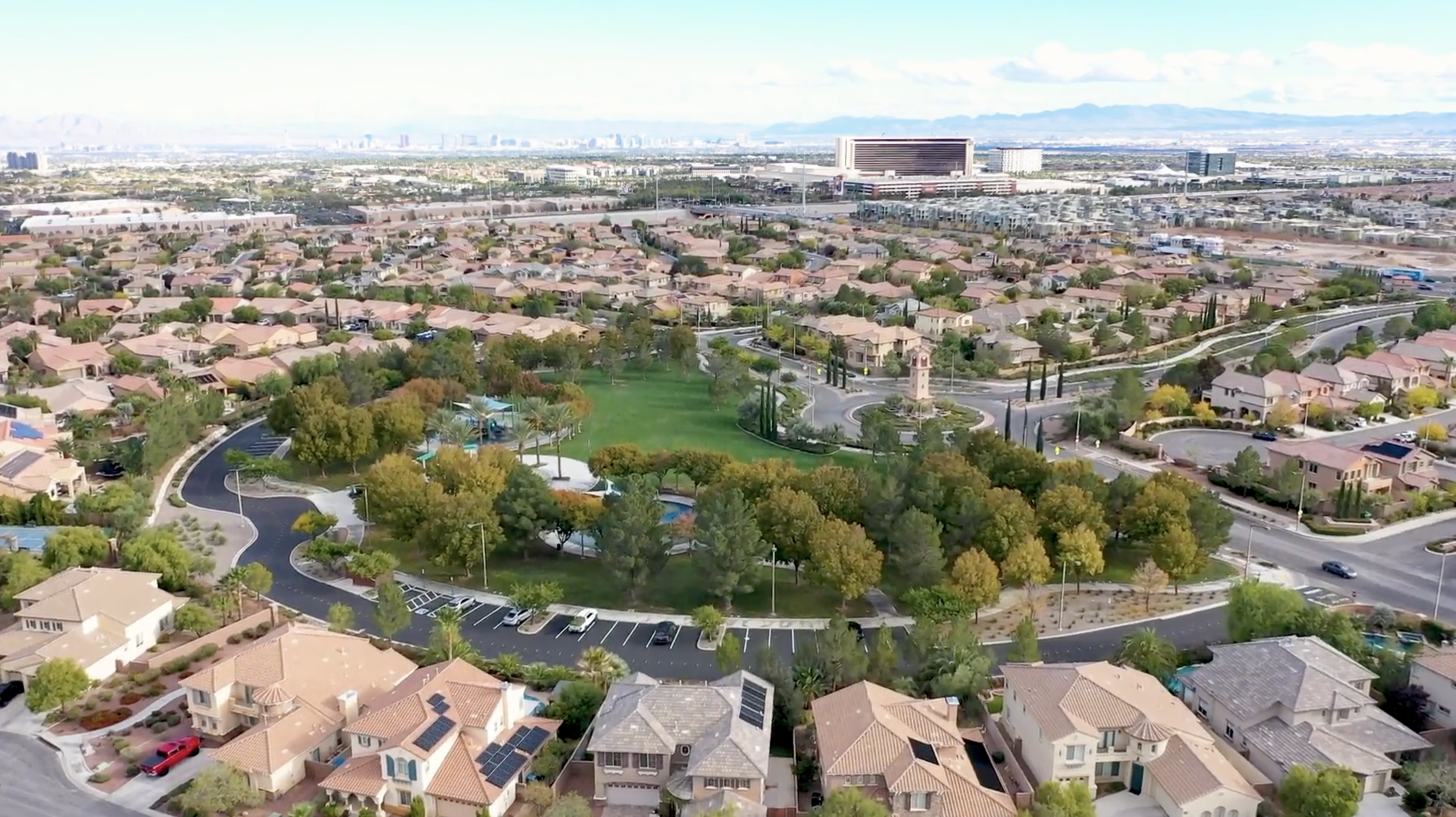 Aerial view of a suburban neighborhood with a park, green trees, residential houses, and streets in Las Vegas, Nevada, with mountains in the background.