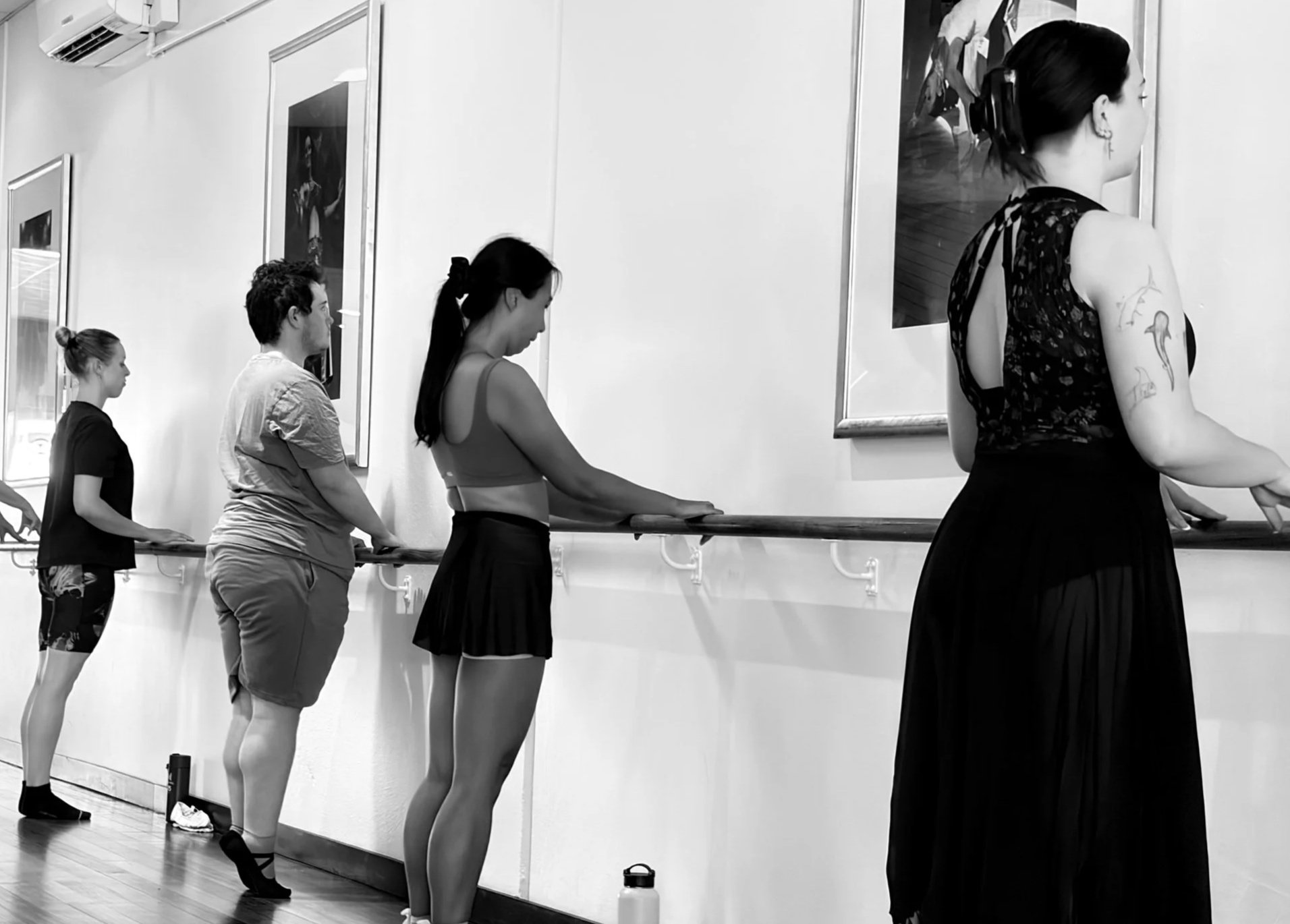 People in a dance class lined up at a barre in a dance studio, practicing ballet.