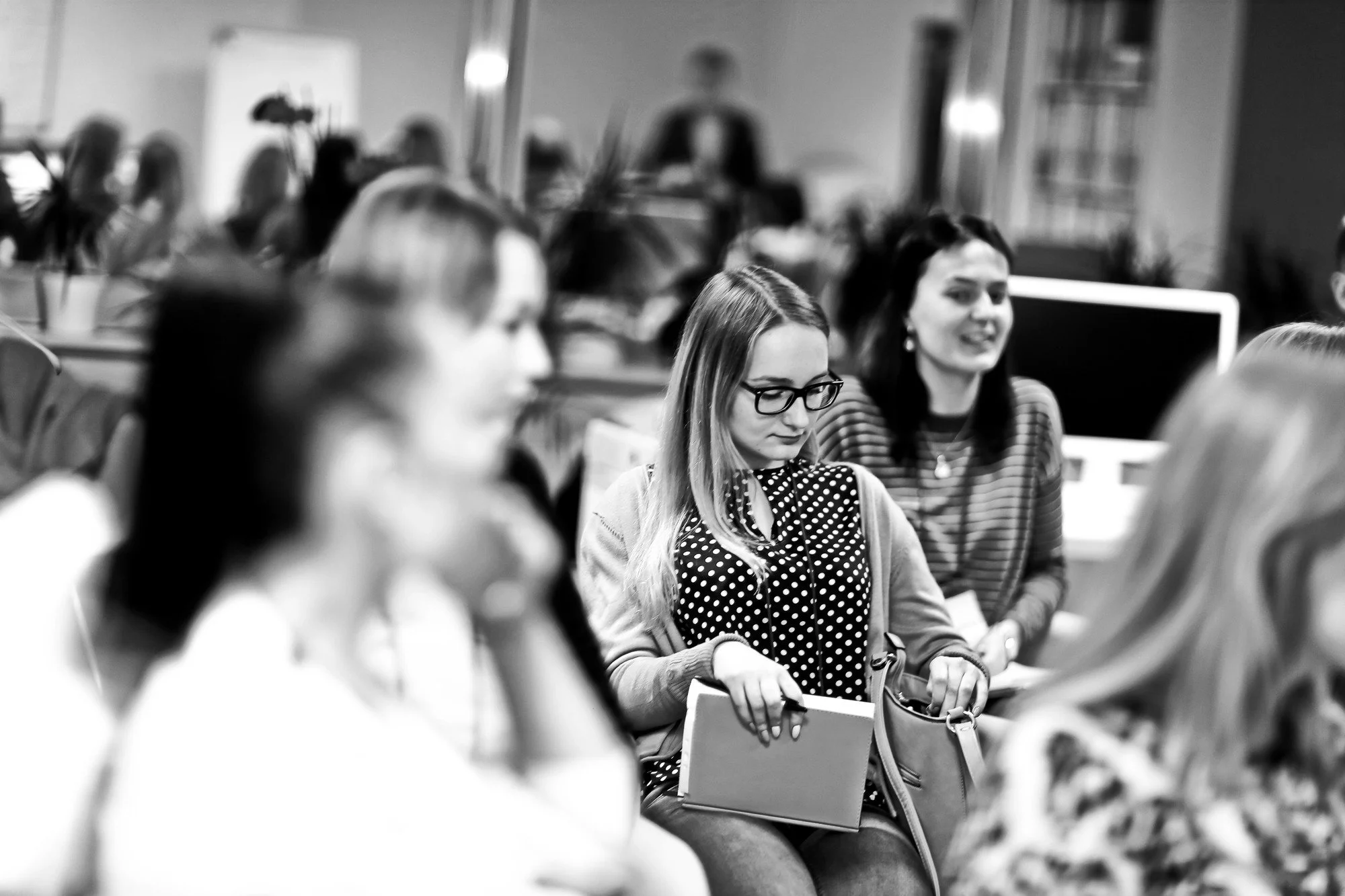 A group of women sitting and listening, with a woman standing at a lectern in the background.