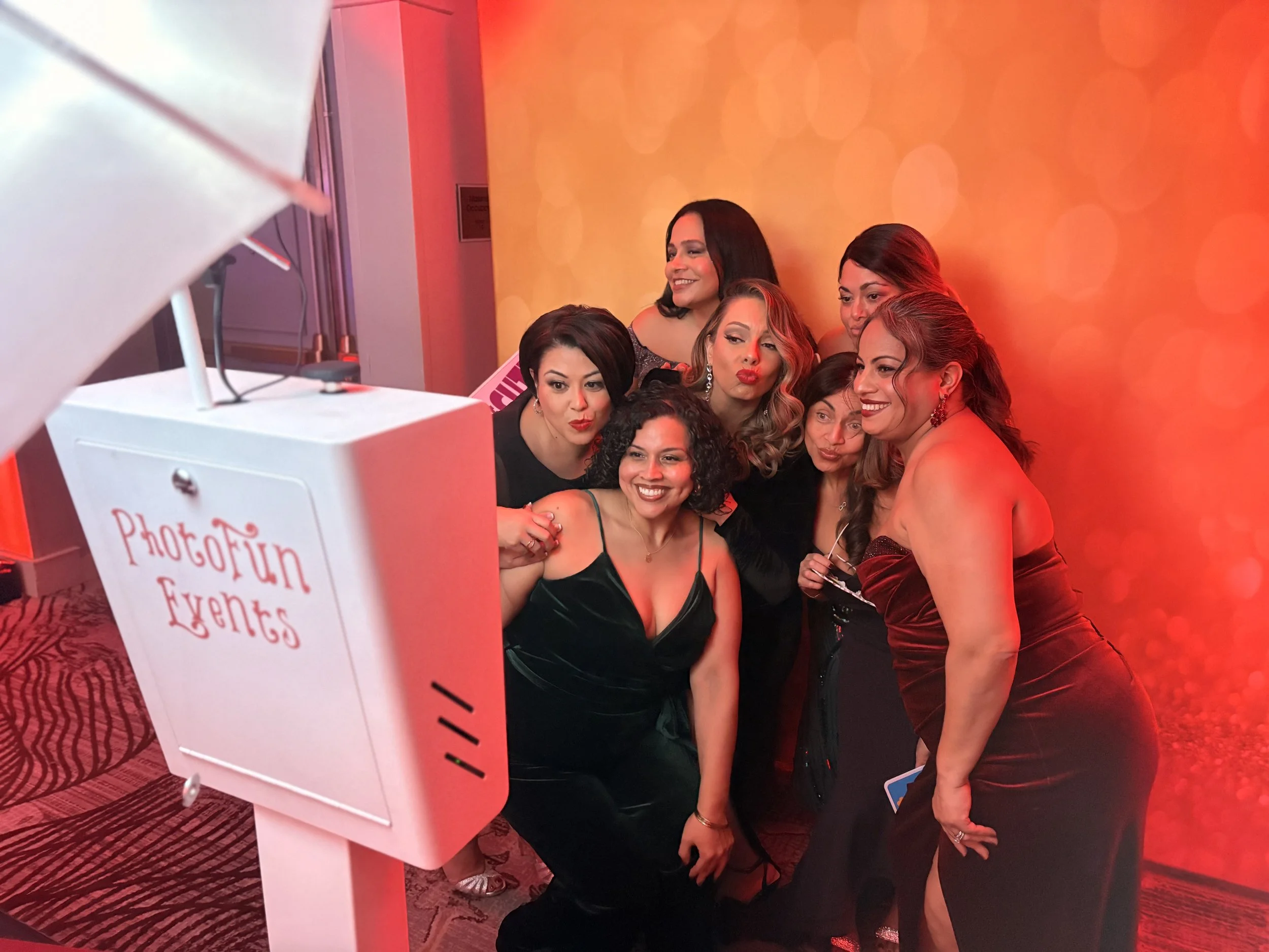 Group of women taking a selfie at a photo booth with a red and orange background.