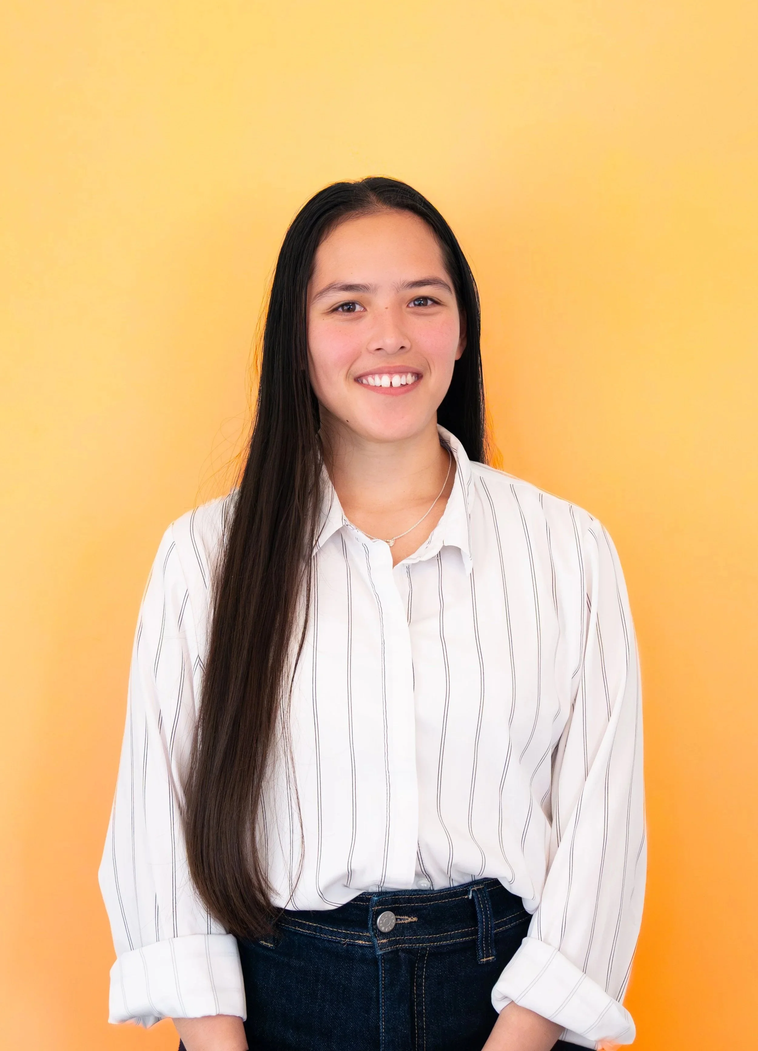 Aaliyah Middleton's profile photo: A young woman, with long dark hair smiling, wearing a white striped shirt and dark jeans, standing against a yellow background.