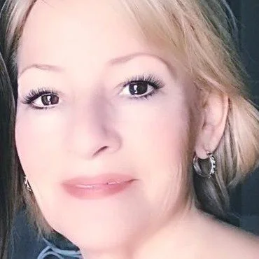 Close-up of a woman with blonde hair and hoop earrings, smiling slightly.