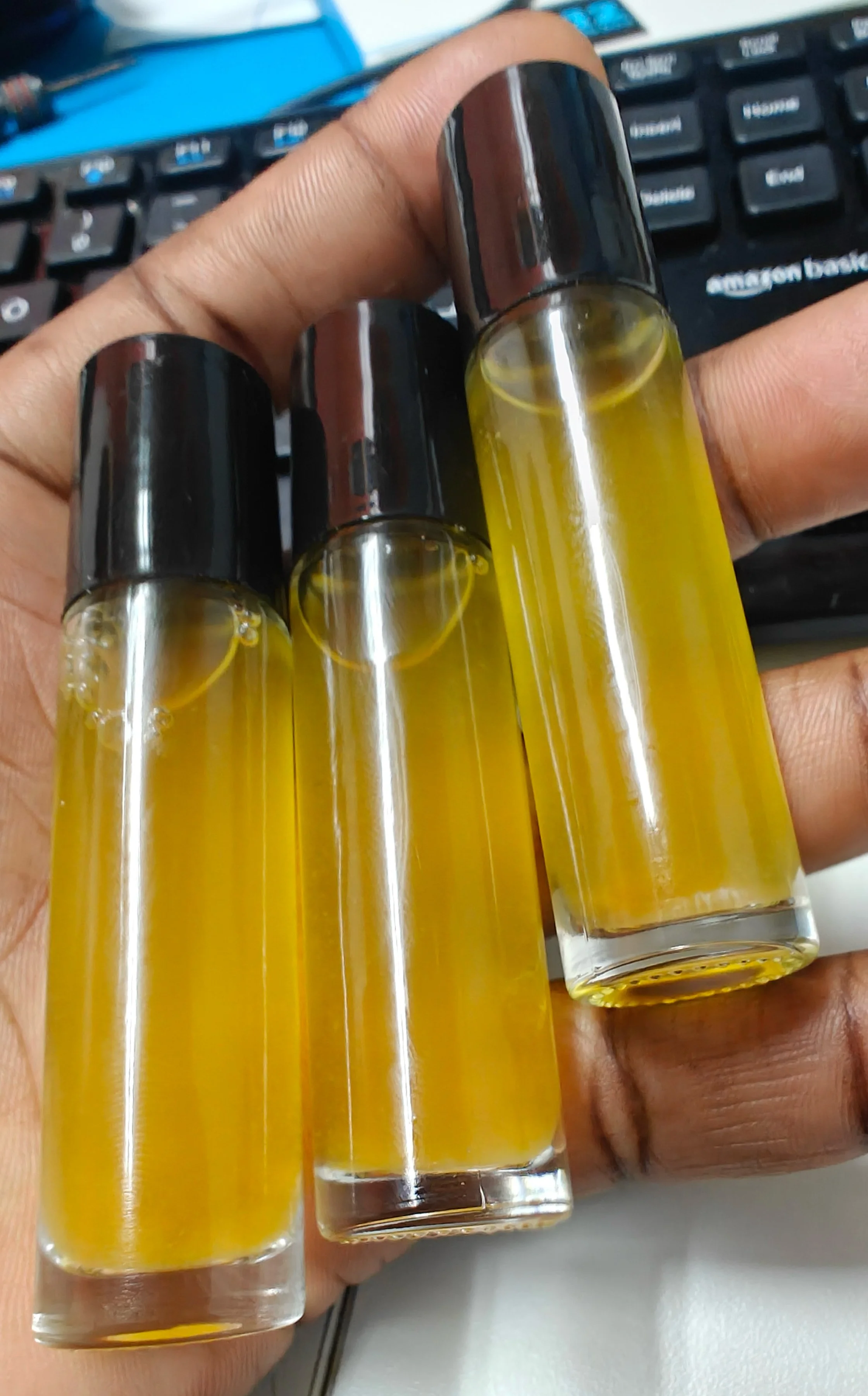 Close-up of three small glass bottles filled with yellow liquid, held in a person's hand over a keyboard.