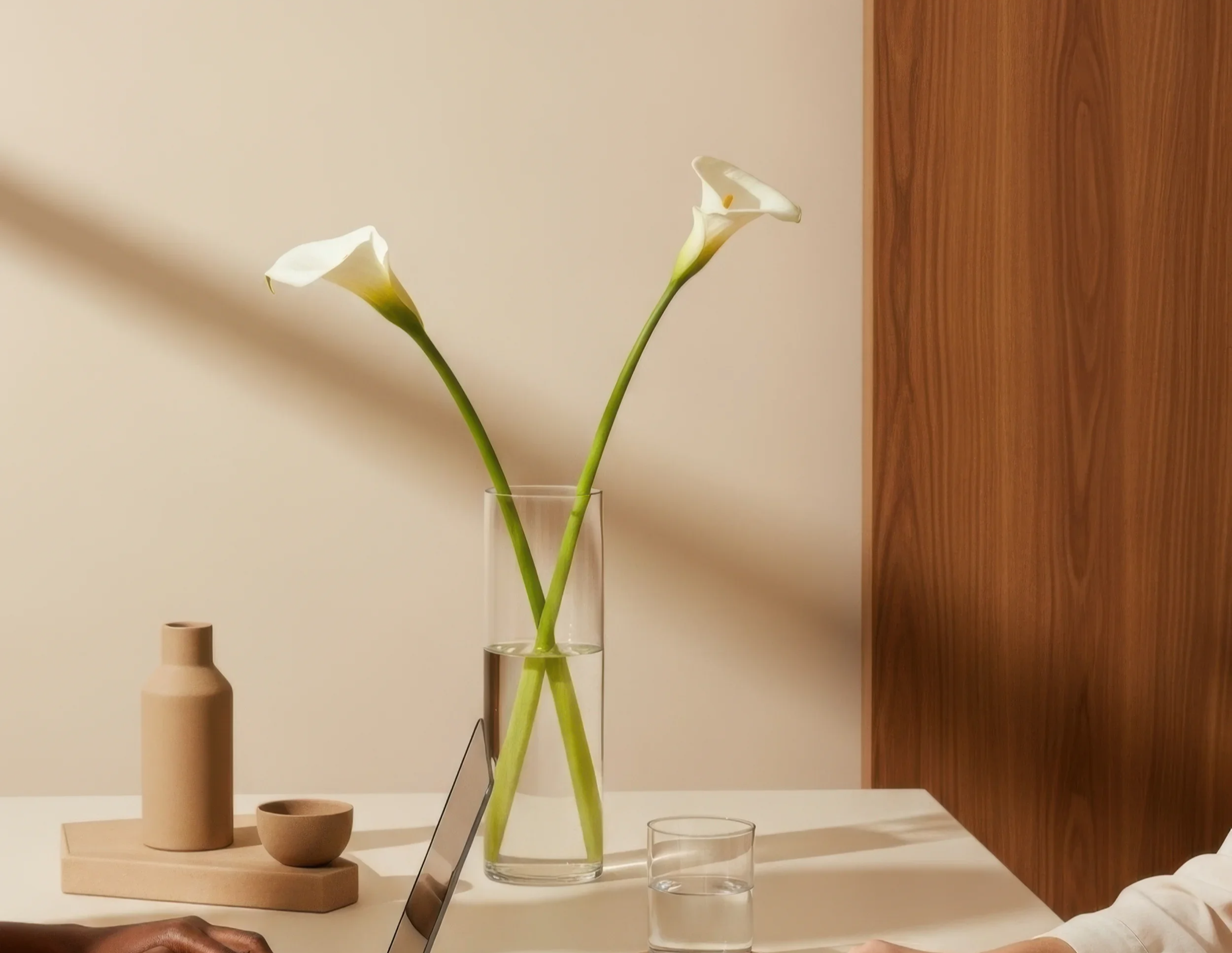Two calla lilies in a glass vase with a zen taupe background. Peaceful organized home.