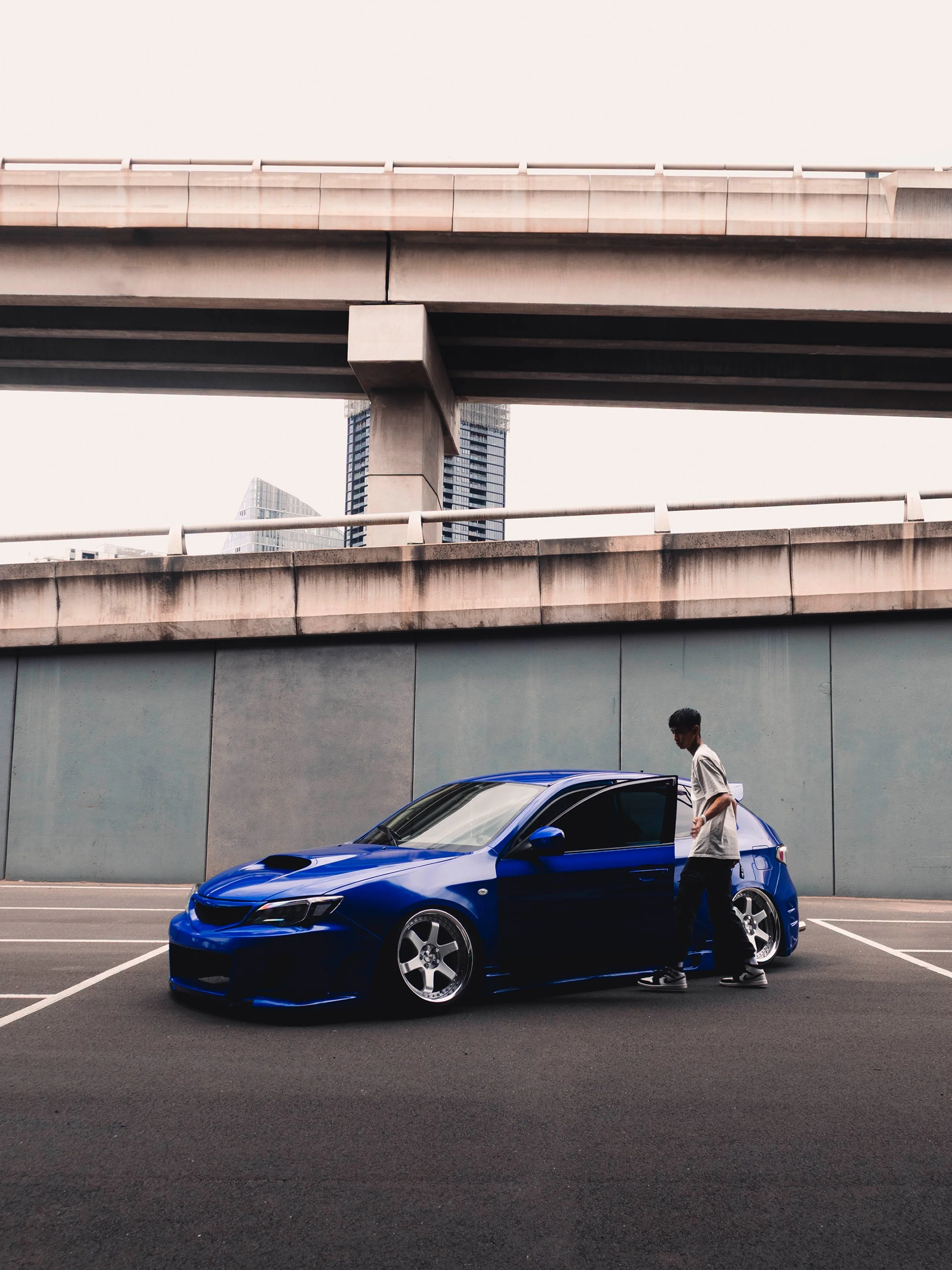 Blue Stanced Subaru WRX parked on an urban street beneath a highway overpass