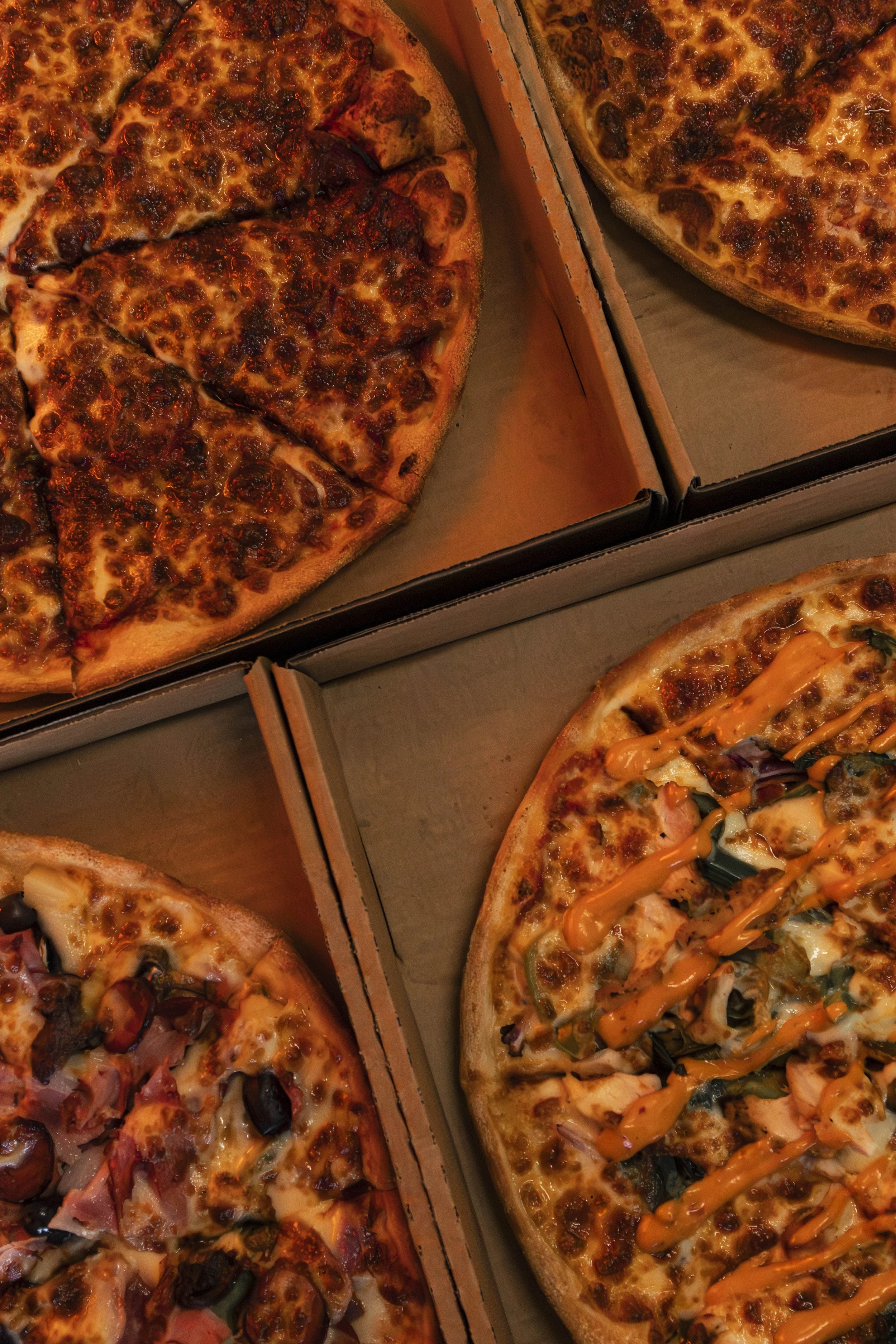 Three different types of pizza in cardboard boxes, topped with cheese and various toppings such as meat, vegetables, and sauces.