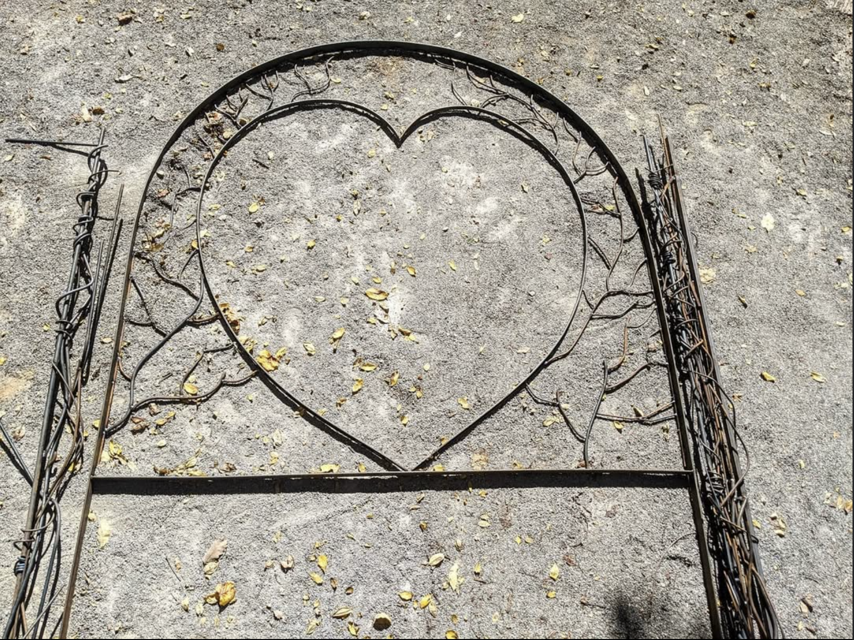 Metal heart-shaped garden trellis on gravel ground with fallen leaves.