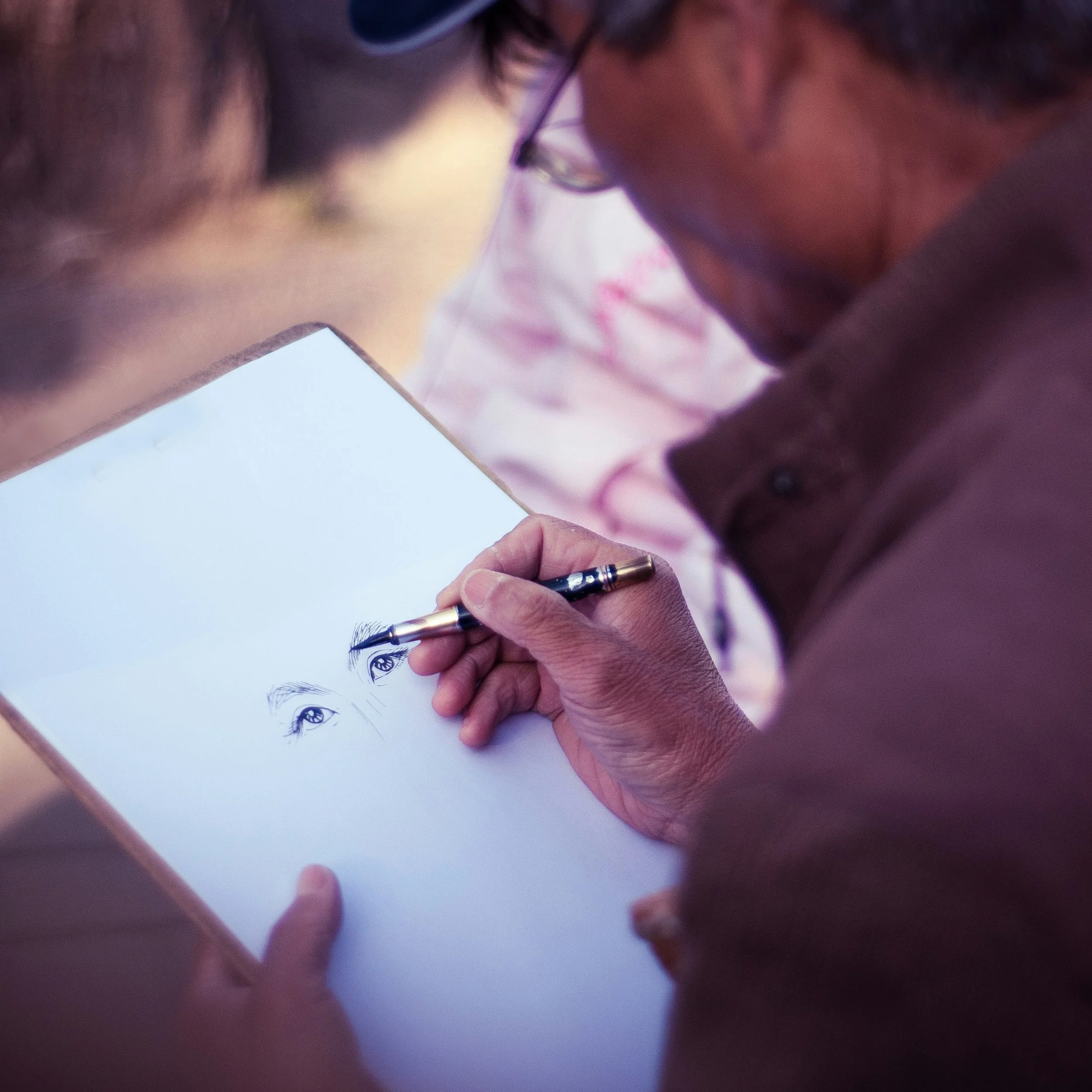 A person drawing a detailed pencil sketch of a woman's eyes on a sheet of paper.