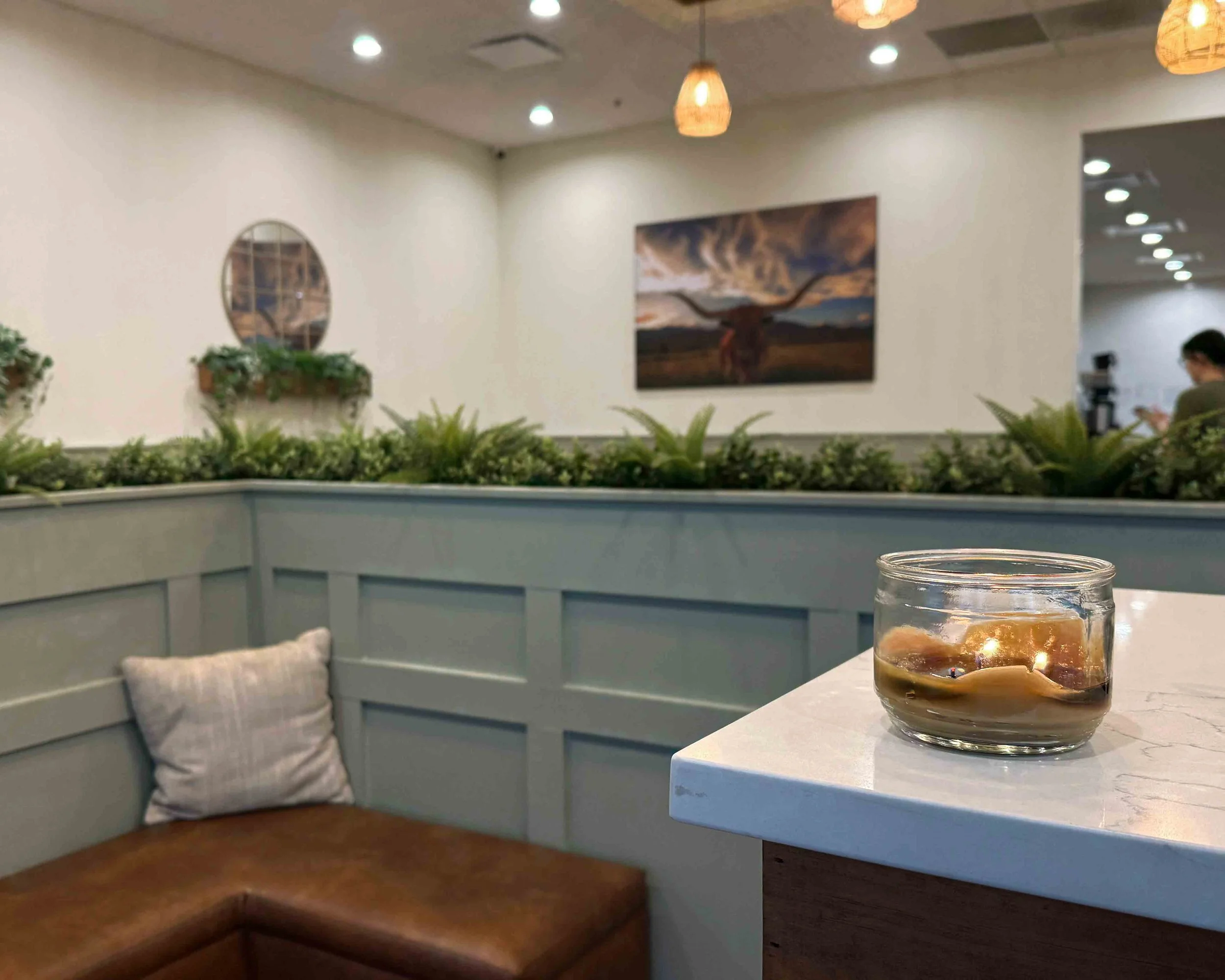 Lit candle on a restaurant counter in a cozy breakfast spot, creating a warm, inviting atmosphere with soft lighting and greenery in the background.