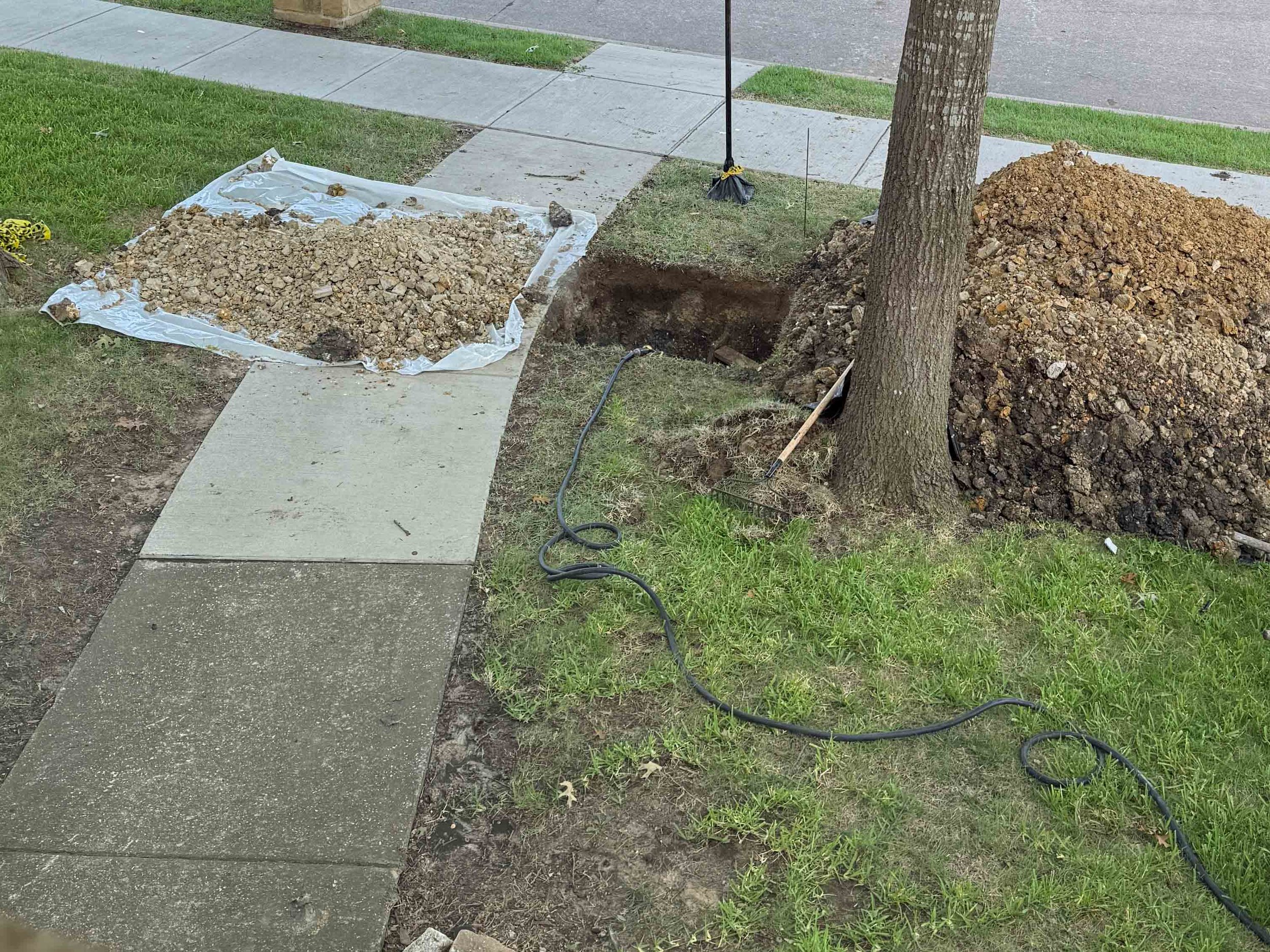 Large excavated hole in a residential yard during a sewer pipe repair.