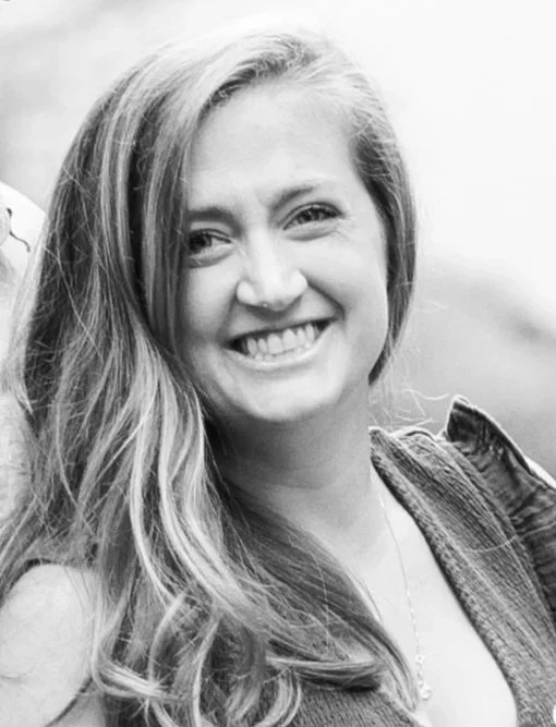 A smiling young woman with long hair looking at the camera, in black and white.