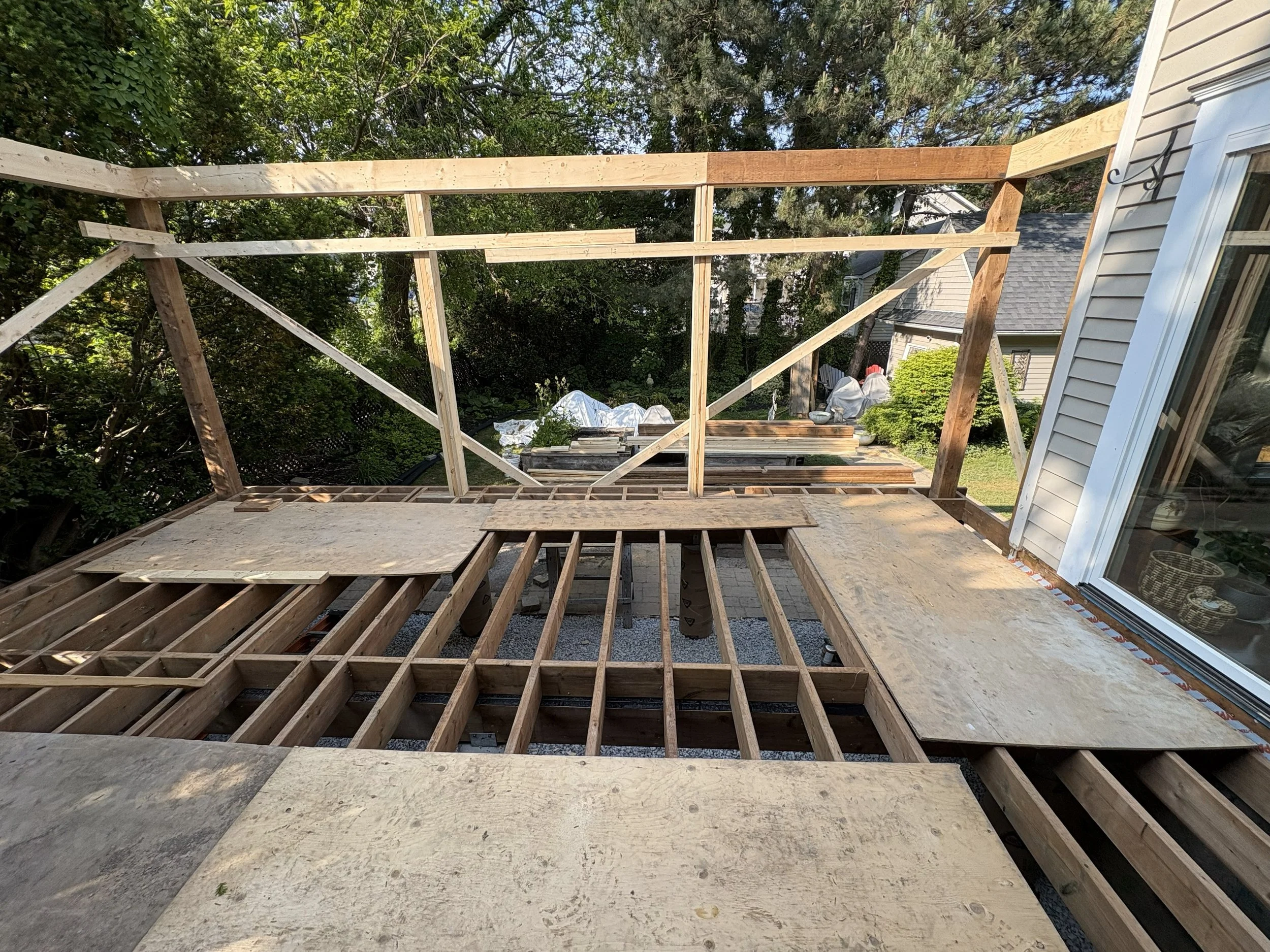 Construction of a wooden deck with framing and partial subfloor in progress at residential backyard