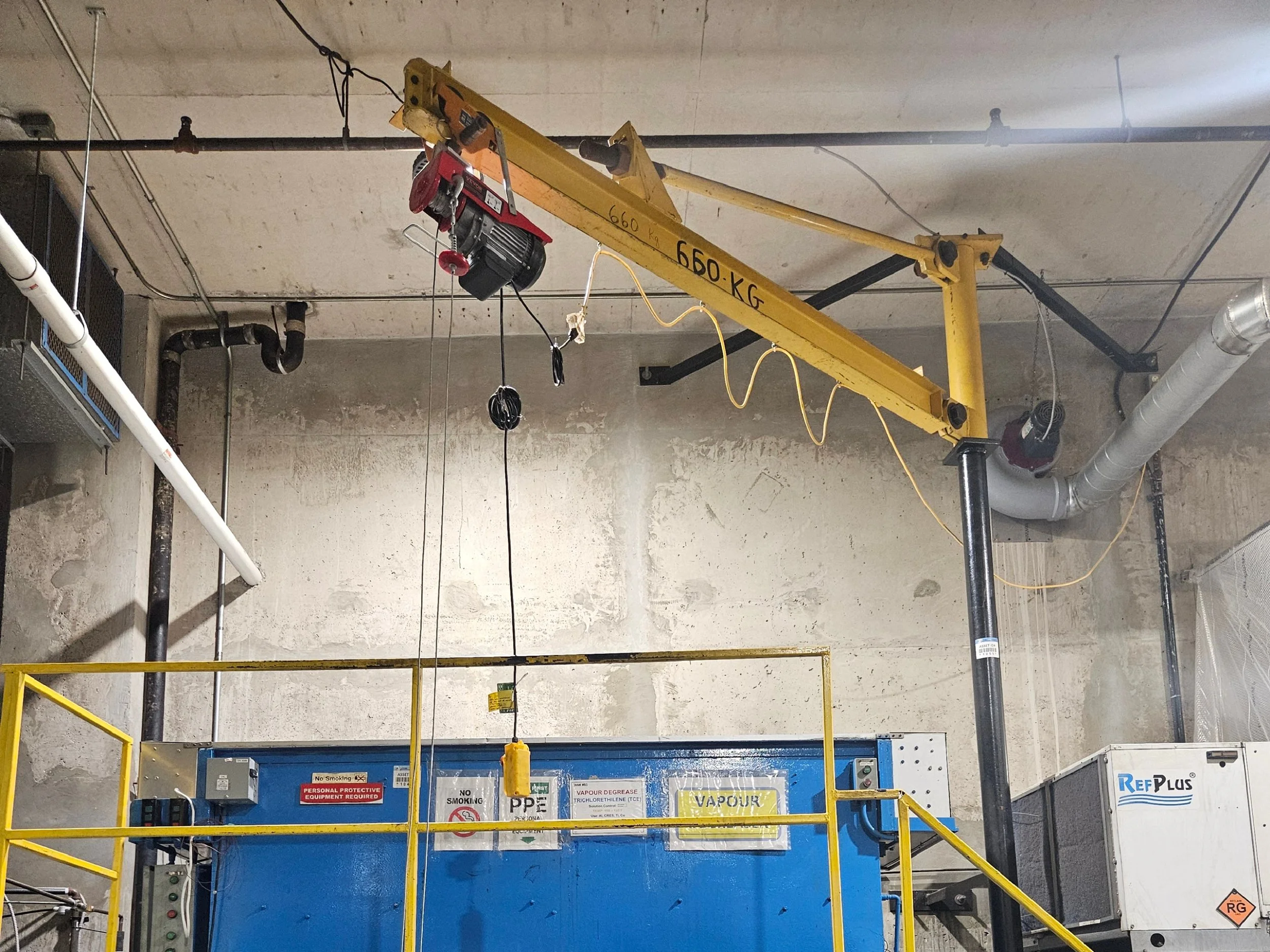 Industrial workspace with large blue machine, yellow overhead crane, and various industrial pipes and equipment.