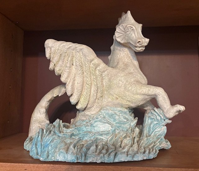 Decorative sculpture of a winged horse on a wooden shelf.