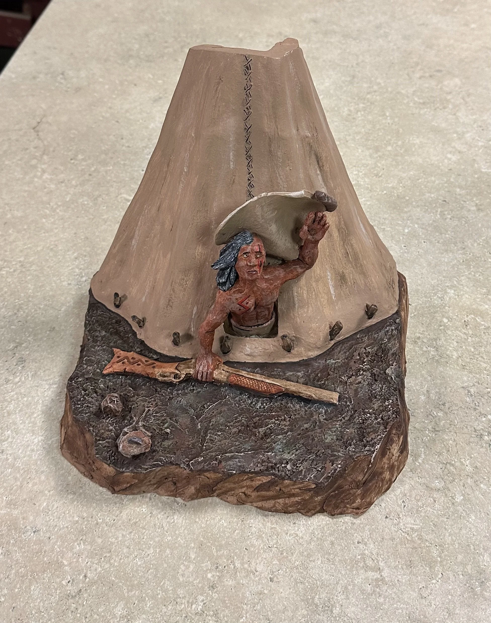 A ceramic sculpture of a Native American mounted on a carved wooden base.