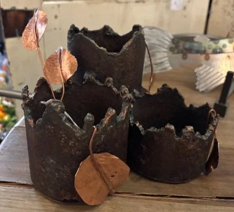 Three metal crown-shaped candle holders with oak leaf decorations on a wooden surface.