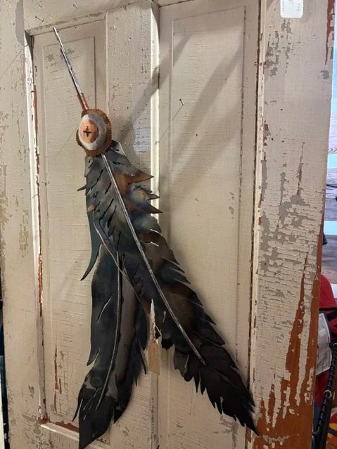 Decorative wall hanging made of black feathers and a wooden stick with a needle on top, hanging on a white wooden door.