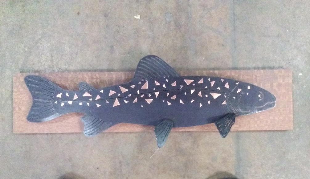 A wooden fish sculpture painted black with white triangular patterns, mounted on a rectangular wooden base.