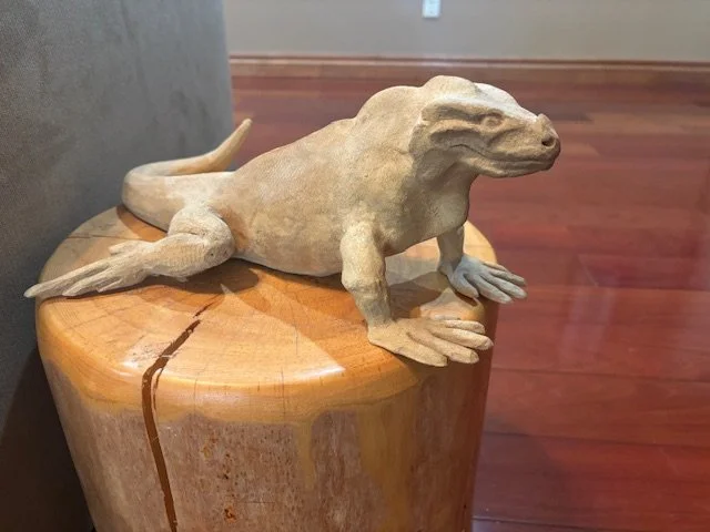 A carved wooden sculpture of a lizard is placed on a round wooden table.