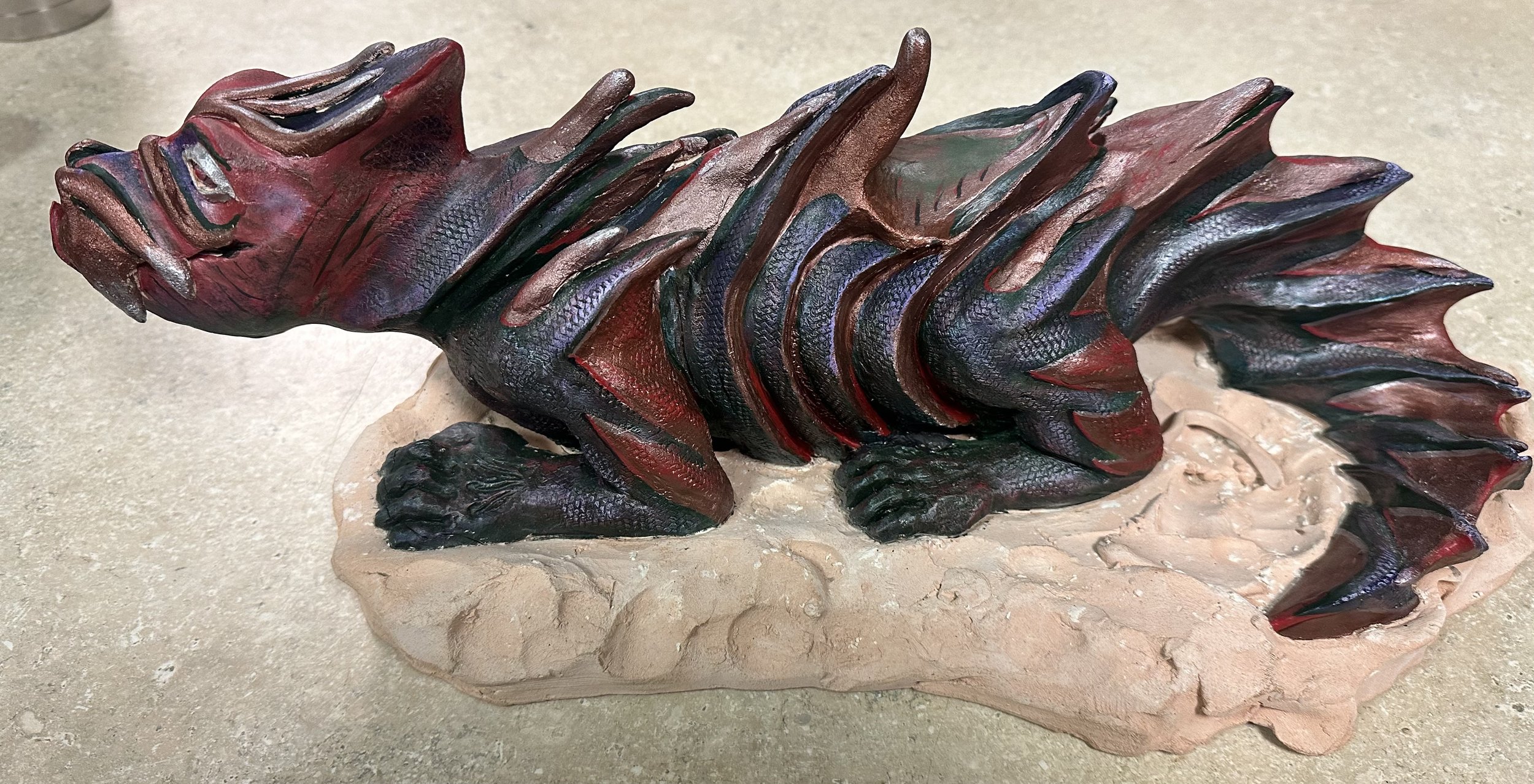 Colorful ceramic sculpture of a dragon, made of painted with textured scales and sharp, pointed features on a beige base.