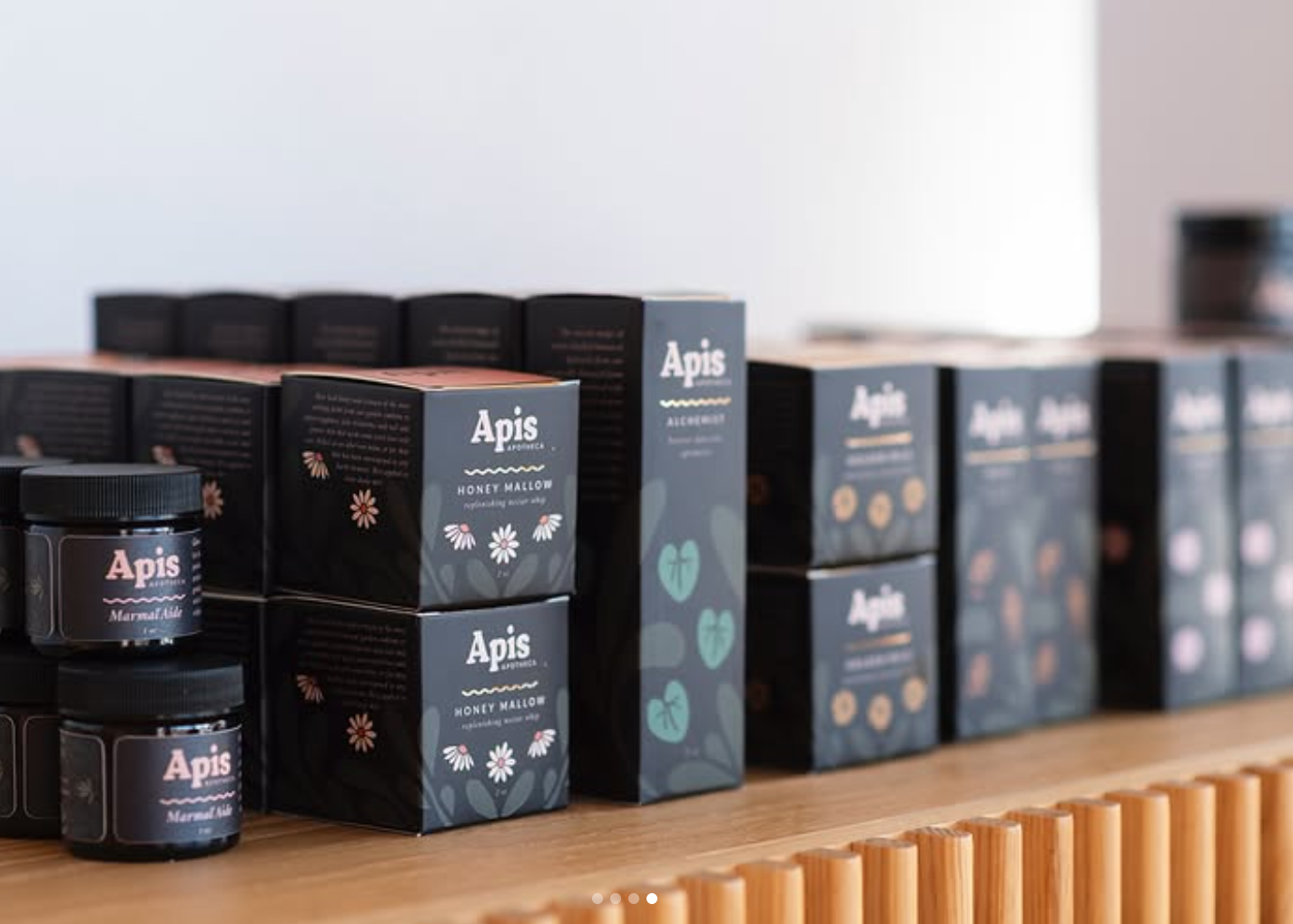 Store display of black and blue boxes and jars of Apis Apotheca herbal skincare products arranged on a wooden surface.