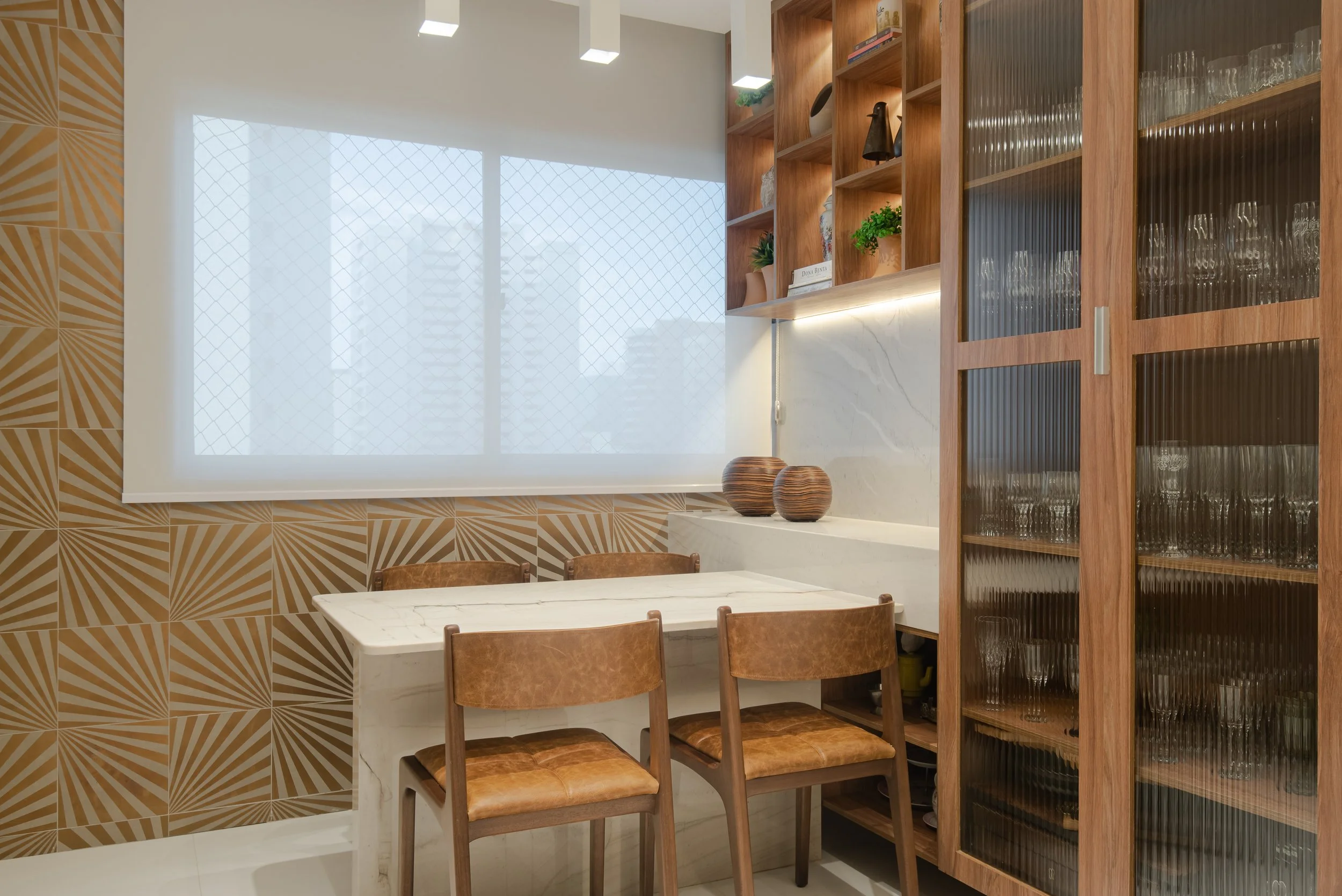 Interior of a dining area with a marble table, wooden chairs, decorative shelves, glassware cabinet, and patterned wall design.