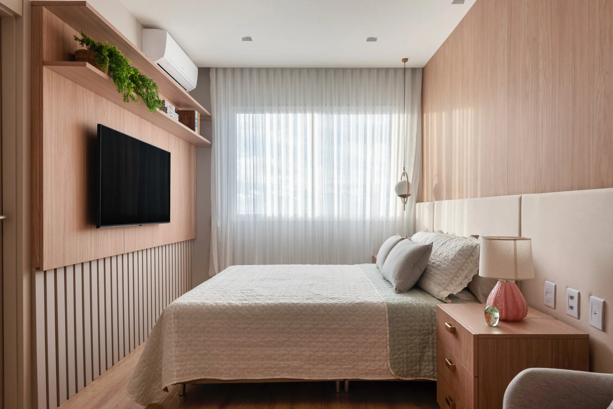 A modern bedroom with a bed, nightstand, and window with white curtains.