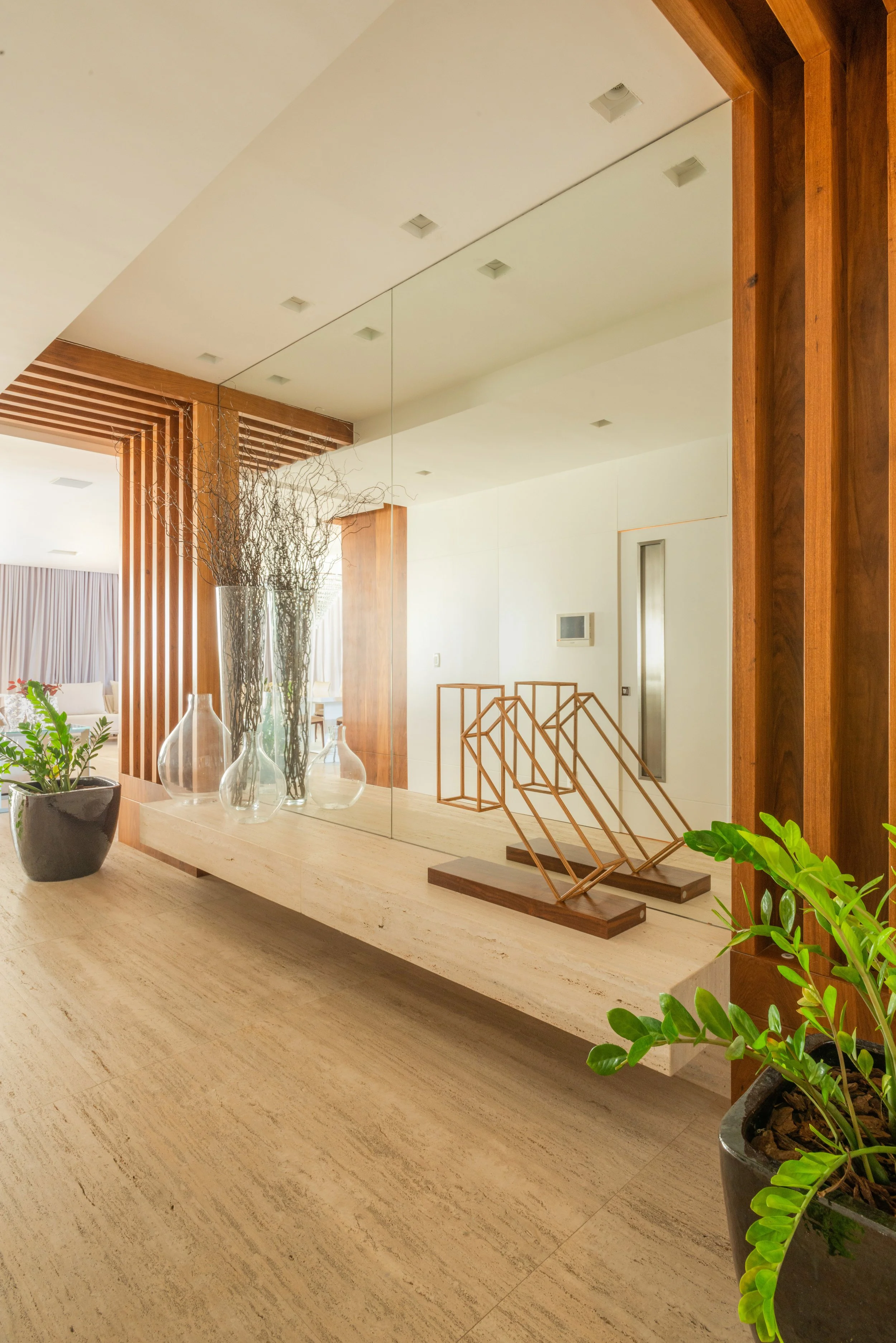 Modern interior with wooden accents, large mirror, glass vases with branches, and potted plants.