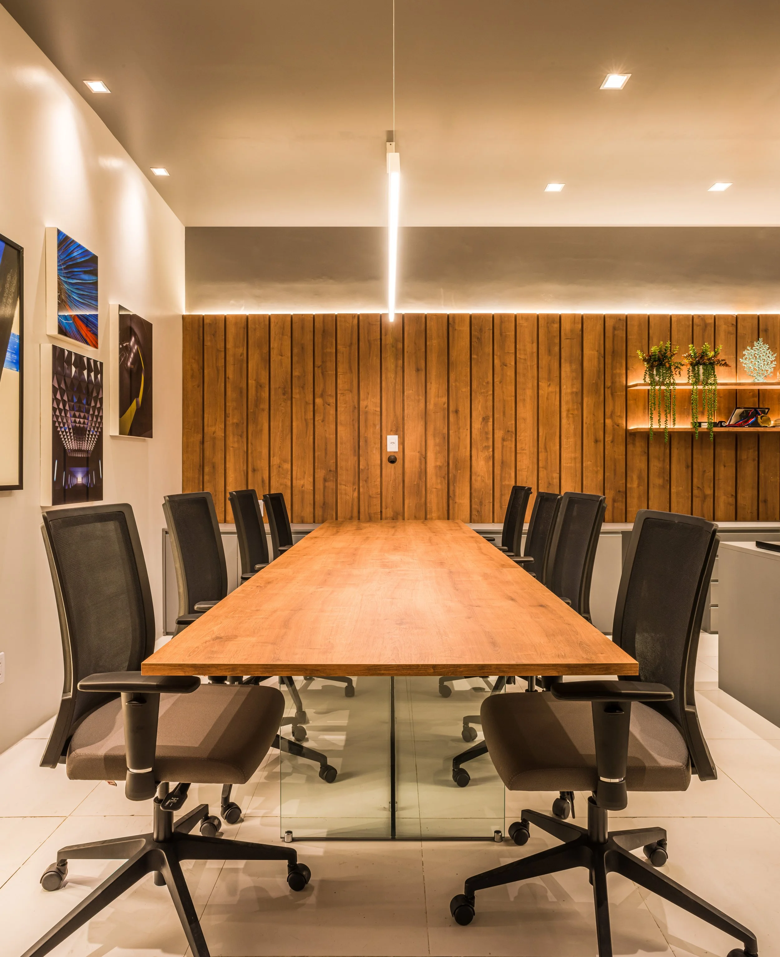 Empty conference room with a long wooden table, black office chairs, wood-paneled wall, and artwork on the white walls.