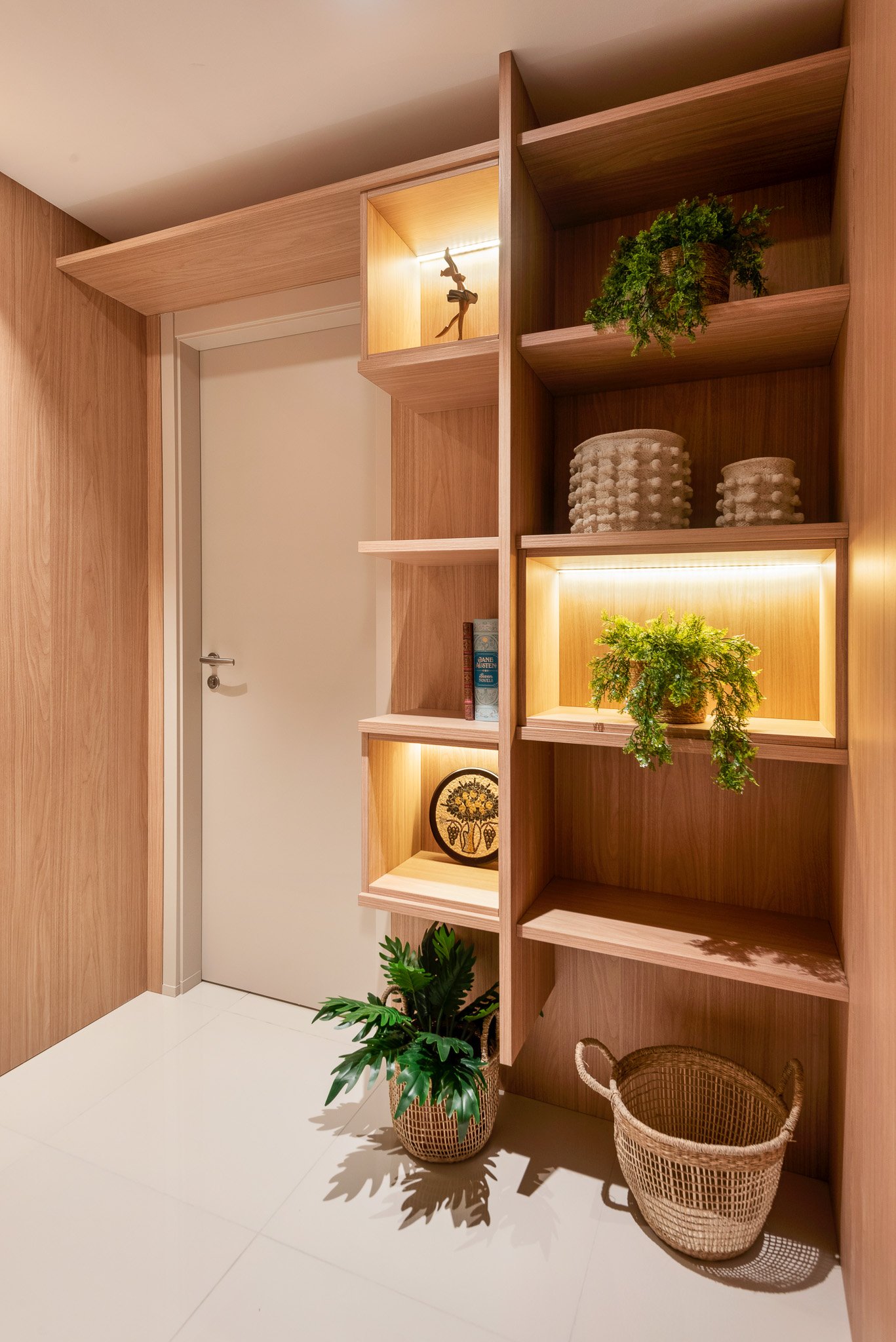 Wooden built-in shelves with decorative items and plants, next to a white door, with two wicker baskets on the floor.