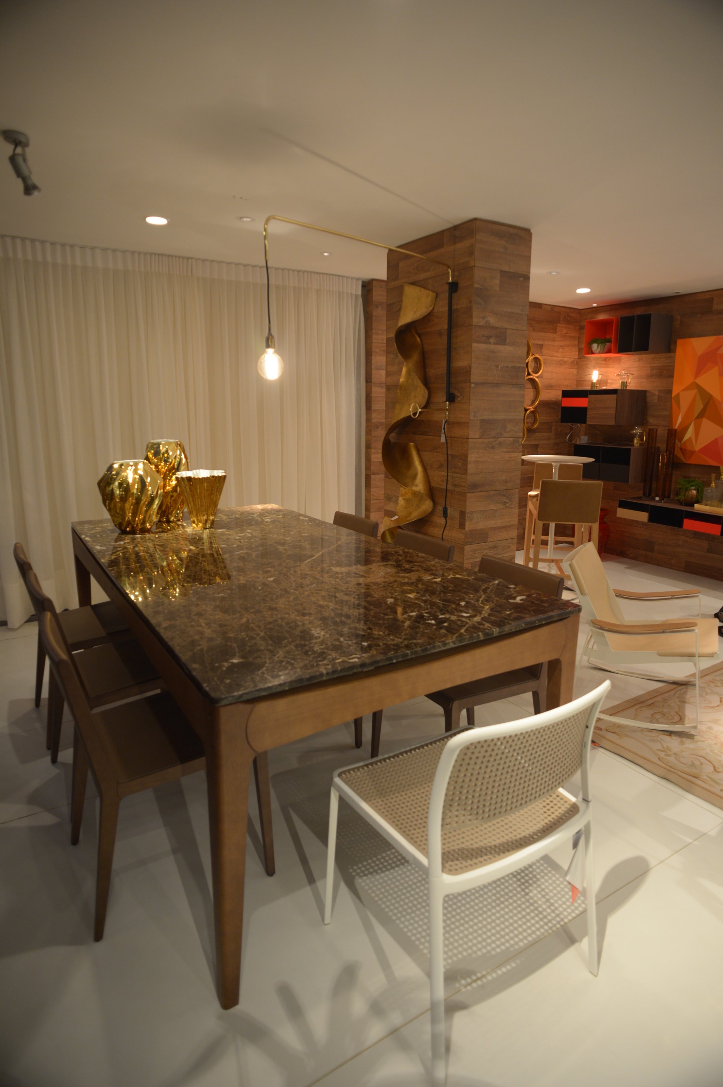 Contemporary dining room with a dark marble table, gold decorative vases, modern chairs, wood-paneled walls, and warm lighting.