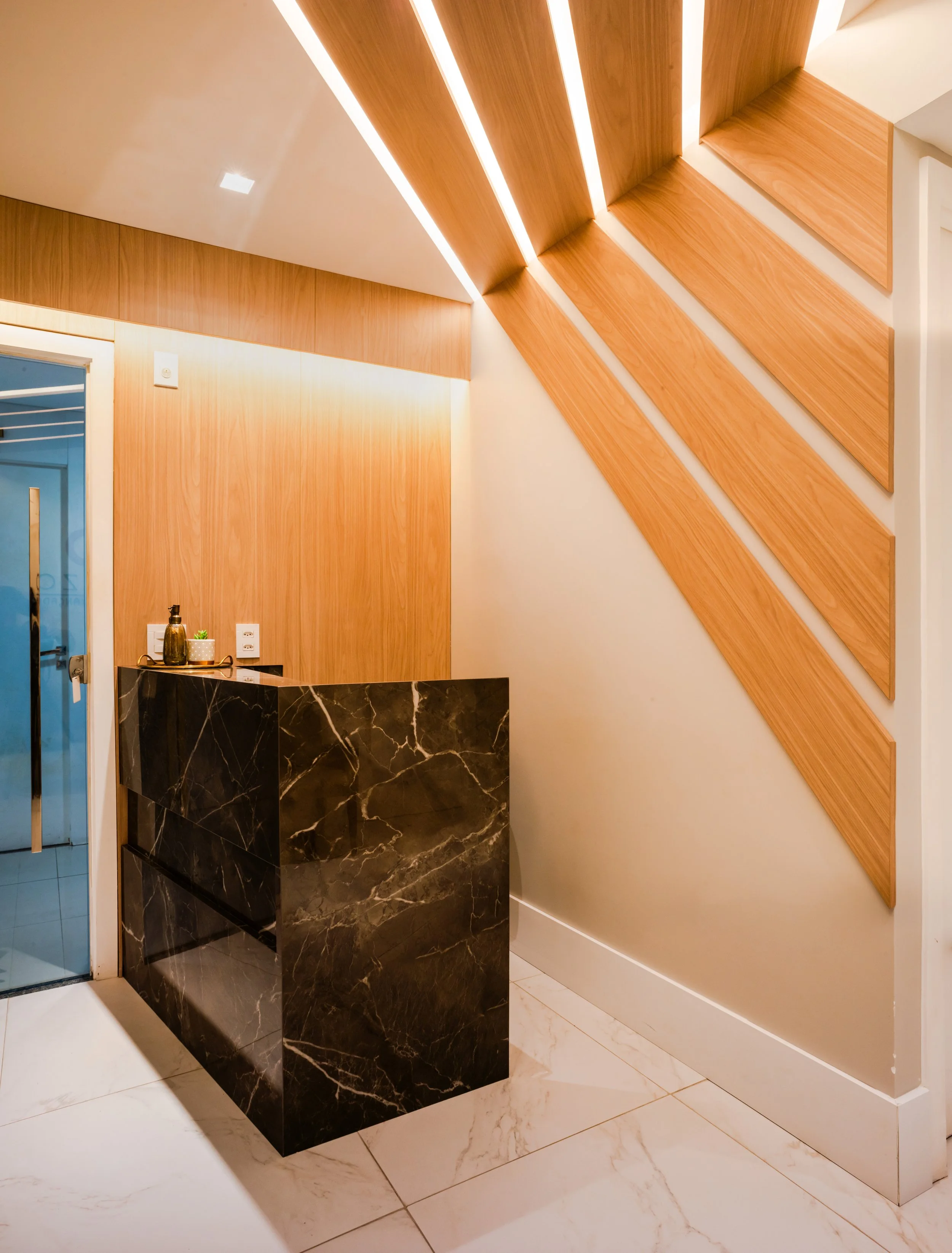 Interior space with a black marble reception desk, wooden wall panels, and a staircase with wooden steps leading upward.
