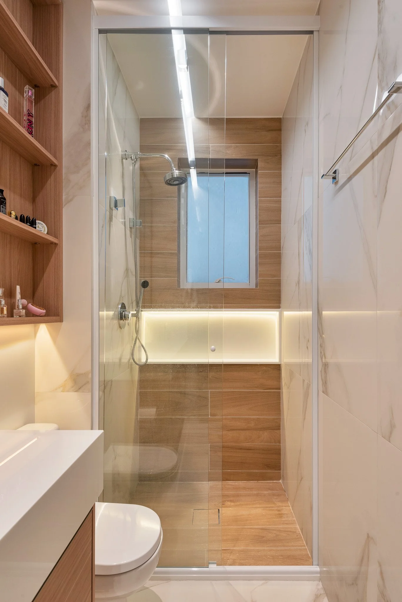 Modern bathroom with a walk-in shower with a glass door, white and wooden accents, a small window, and a white toilet.