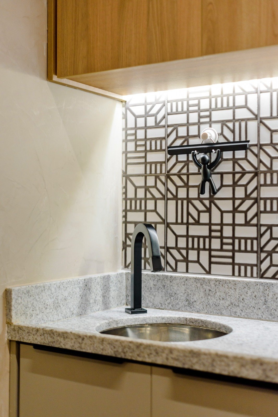 Kitchen countertop with a black faucet, decorative backsplash tiles, and a wall-mounted hook holding a small scale.