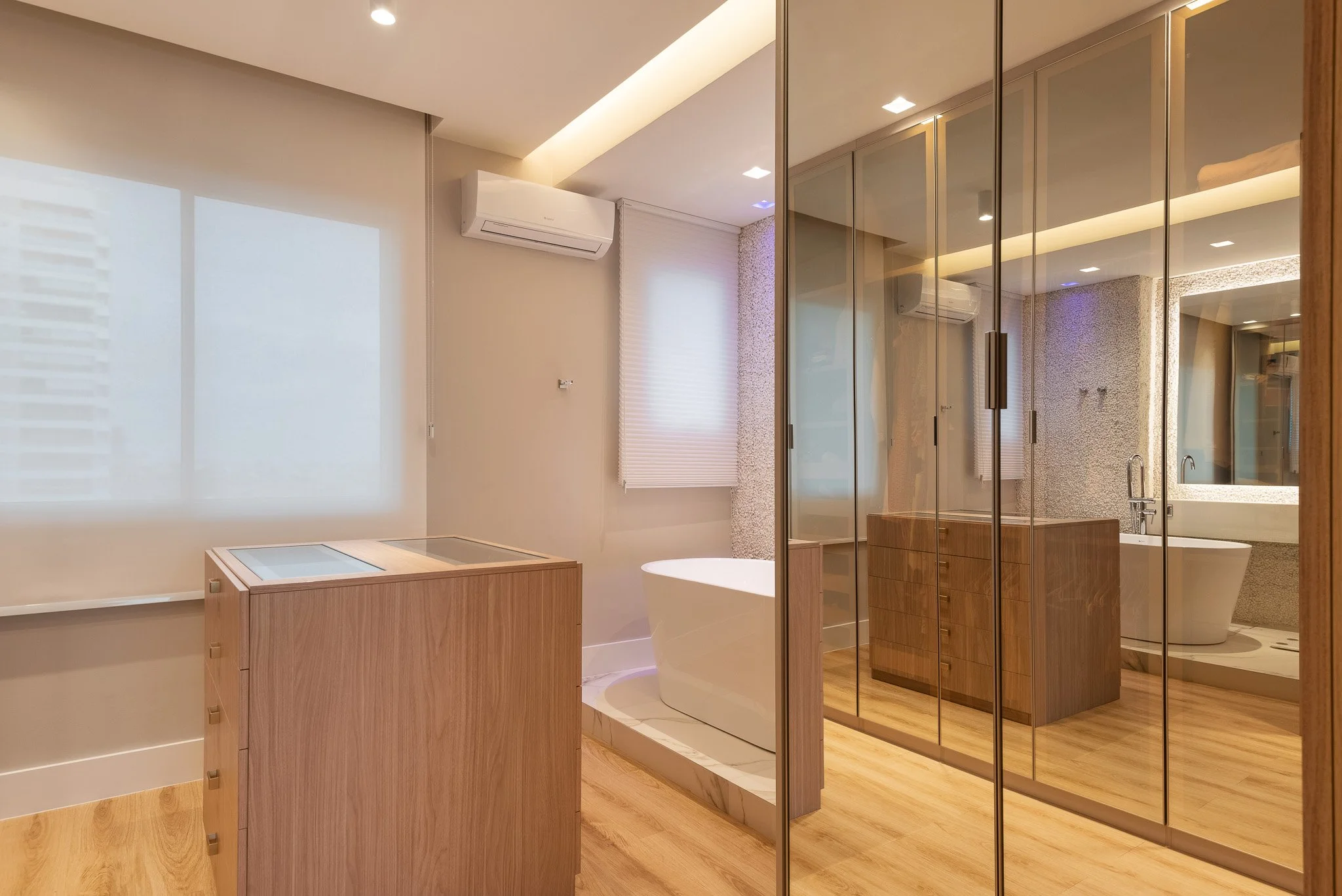 Modern bathroom with wooden flooring, glass shower enclosure, freestanding bathtub, wooden vanity, and large mirrored closet doors.