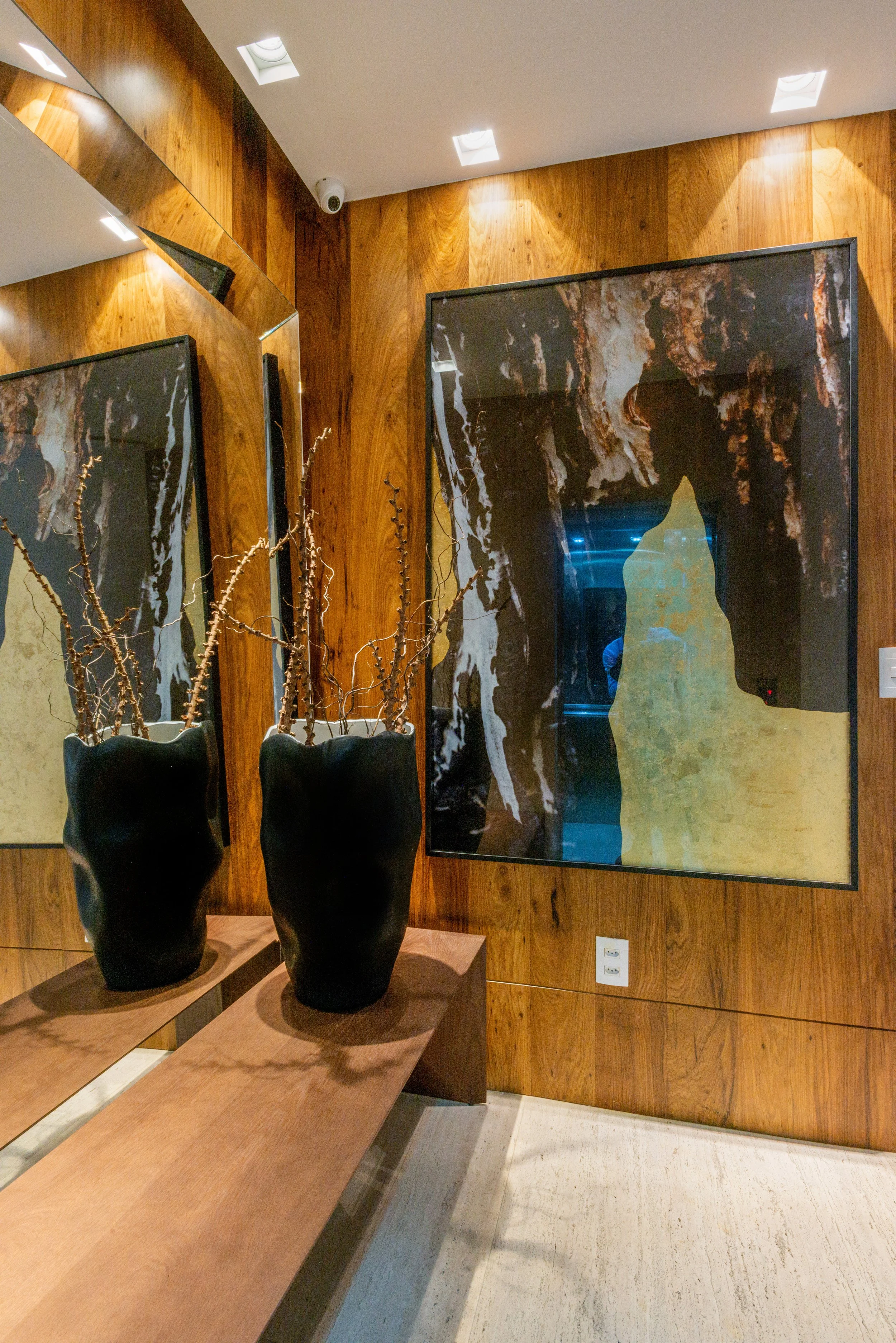 Interior of a room with wood-paneled walls, two black vases with dry branches, and abstract artwork on the wall.