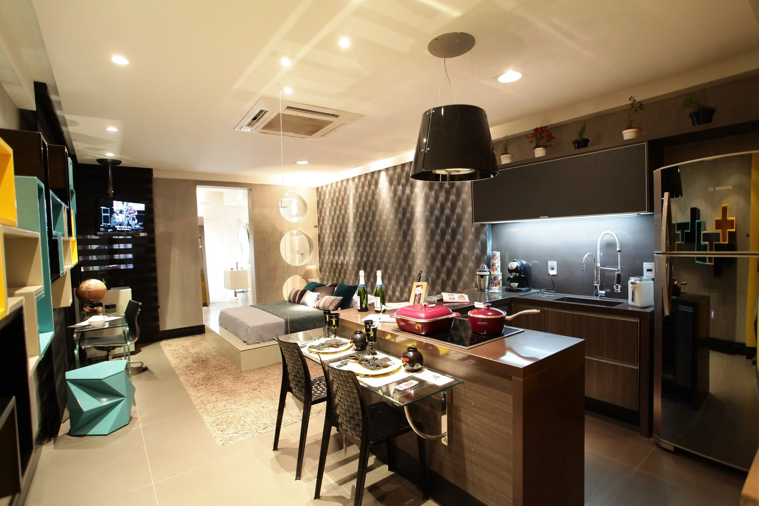 Modern open-concept apartment living room and kitchen with breakfast table, sofa, colorful shelves, and kitchen appliances.