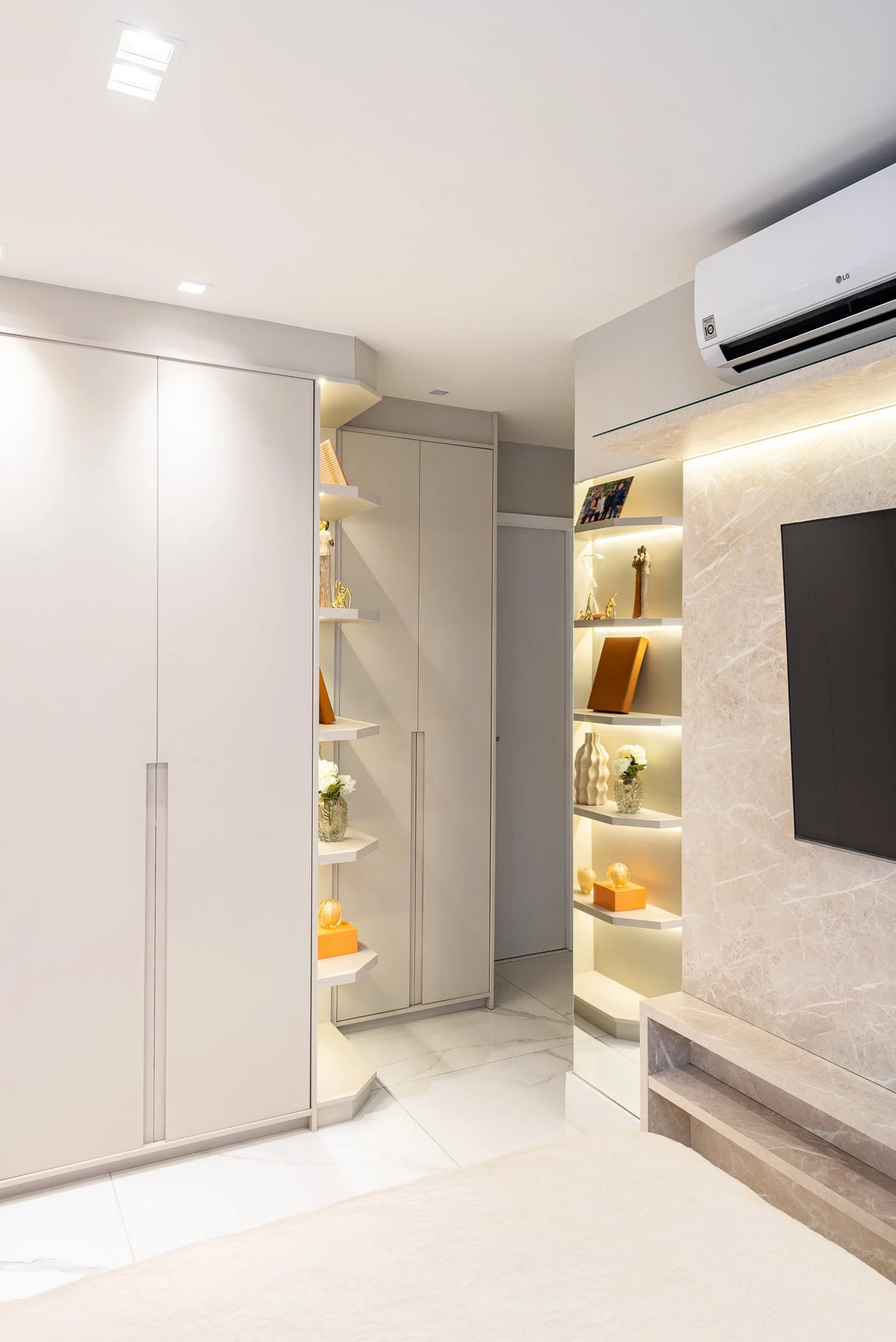 Interior of a modern living room with white built-in shelves, decorative items, and a wall-mounted TV, with an air conditioning unit on the ceiling.
