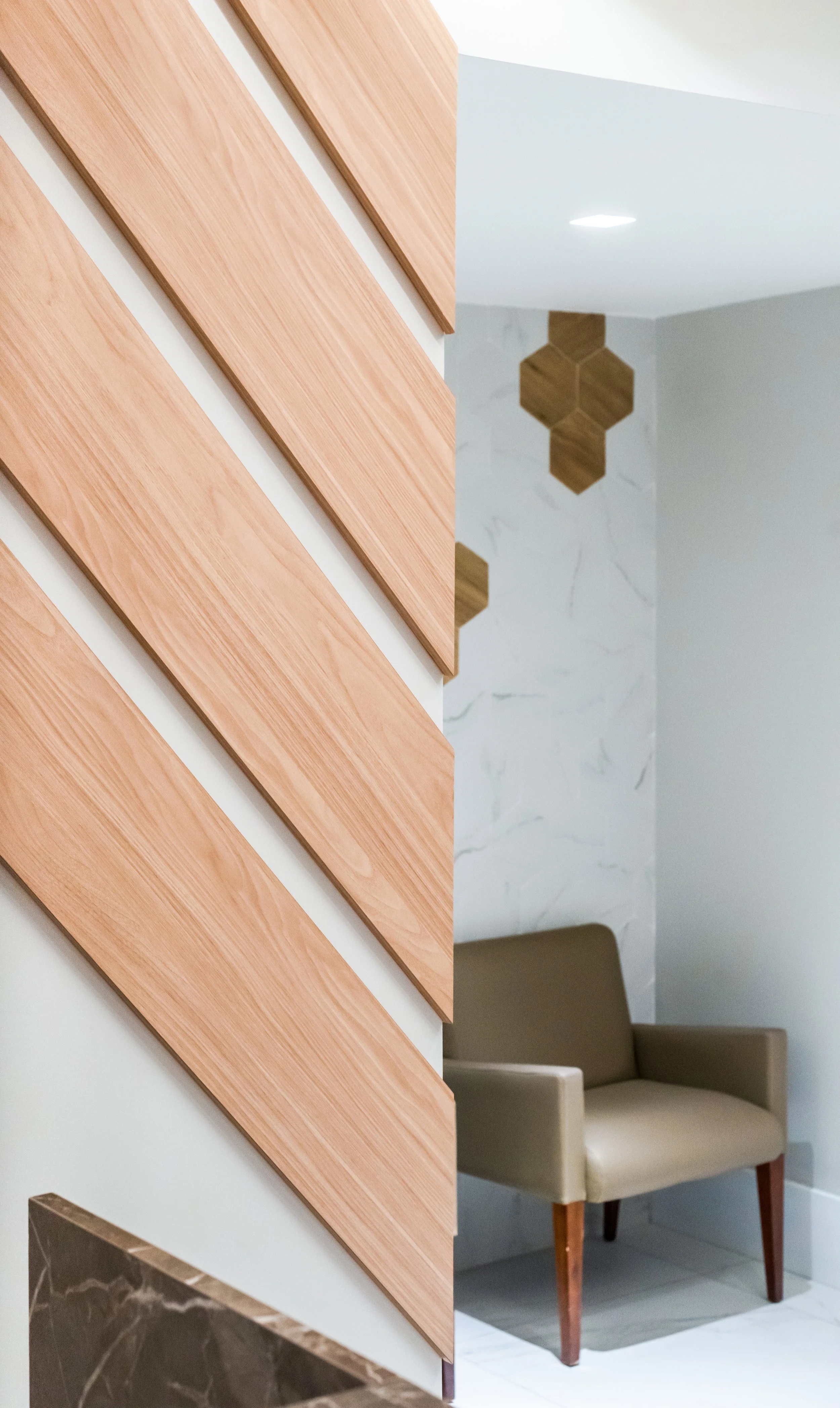 Interior space with a wooden slatted partition, a beige armchair, a marble wall, and decorative wooden wall accents.