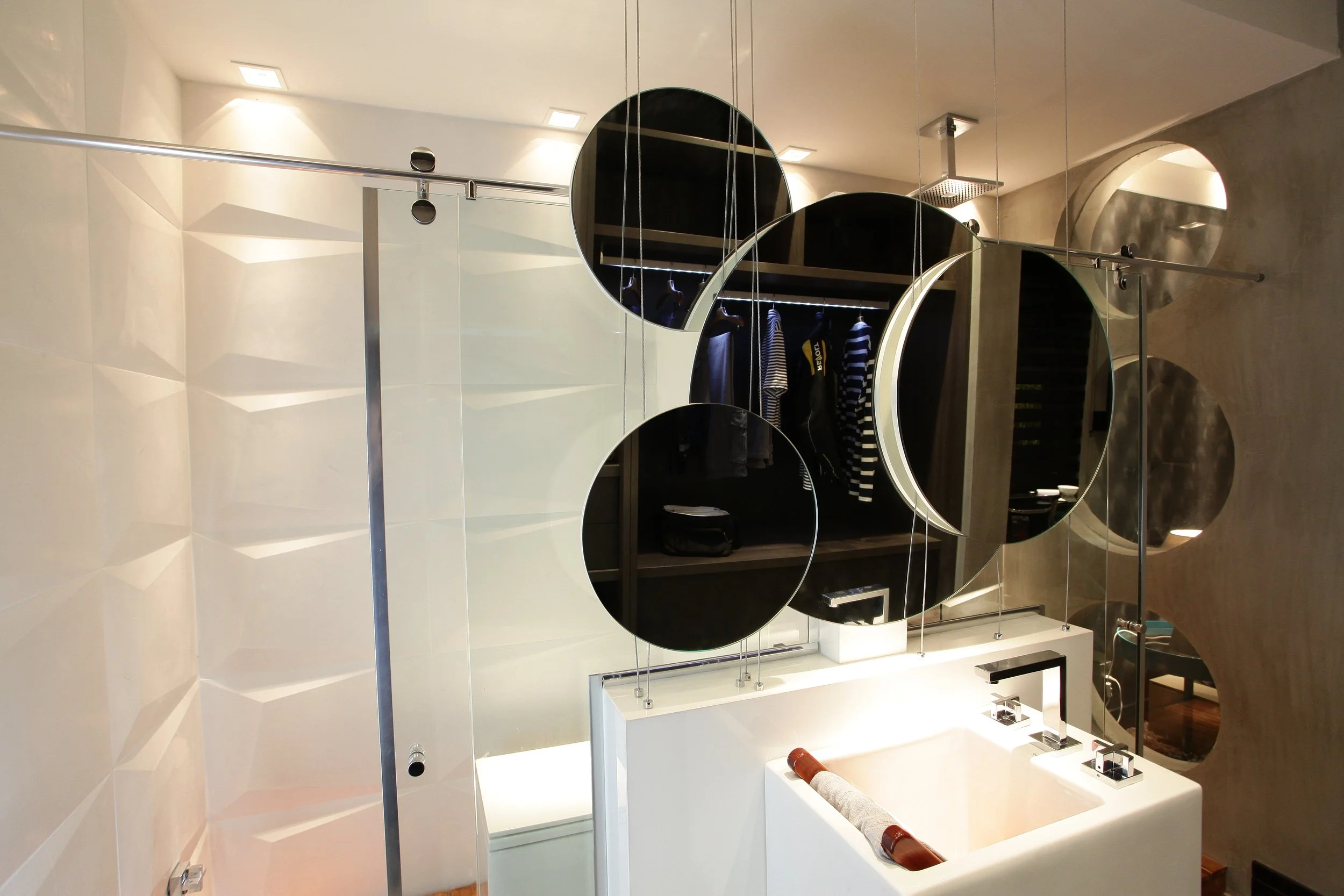 Modern bathroom with a white sink, black mirrored circles on the wall, and a walk-in shower with glass partition.