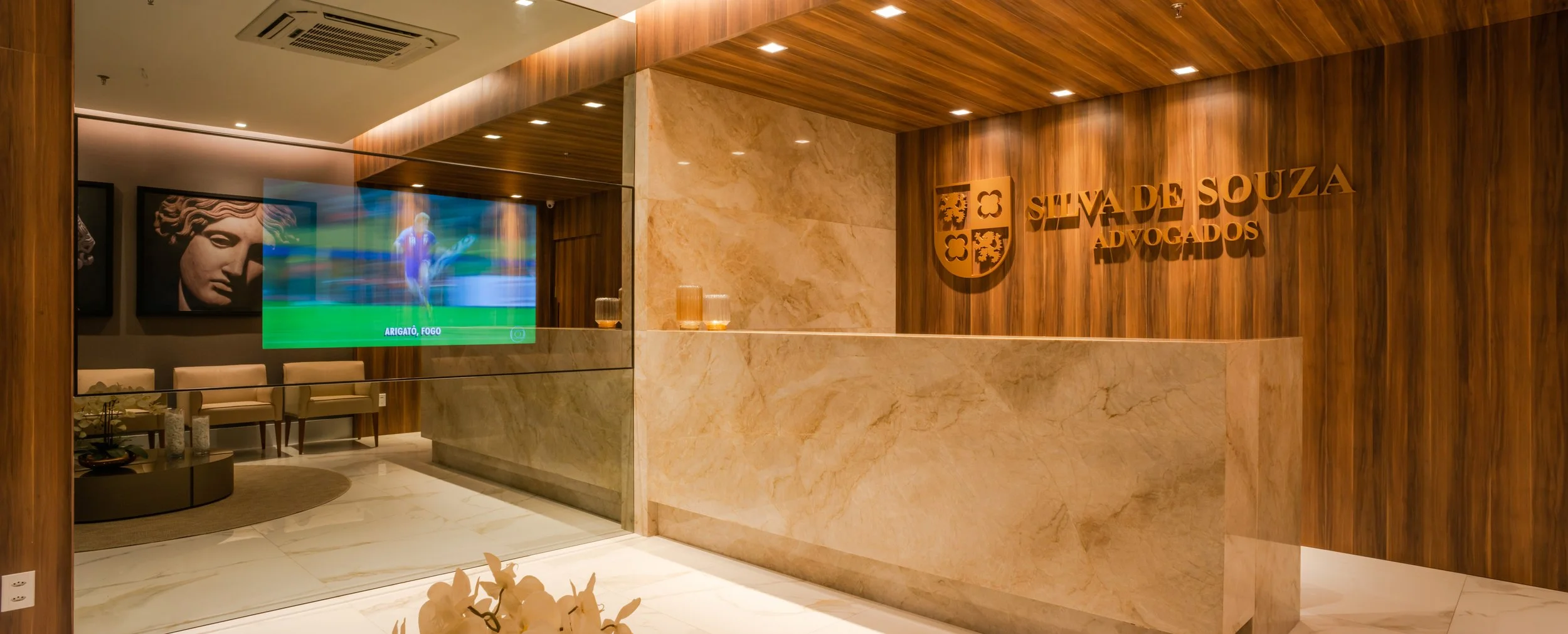 Reception area with wood-paneled walls, a marble front desk, a flat-screen TV showing a sports scene, and artwork of classical sculptures.