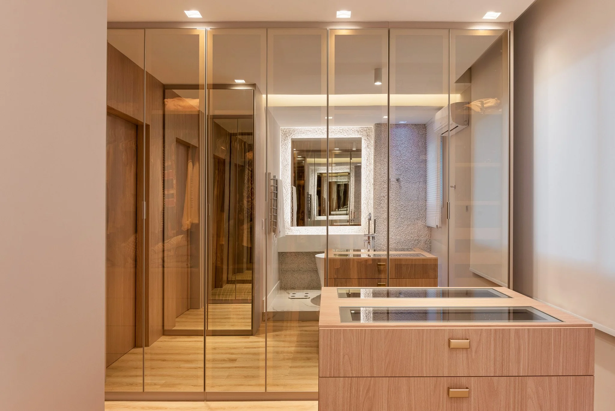 Modern bathroom with mirrored closet doors, a wooden vanity with a sink, a large mirror, and a textured wall with a window.