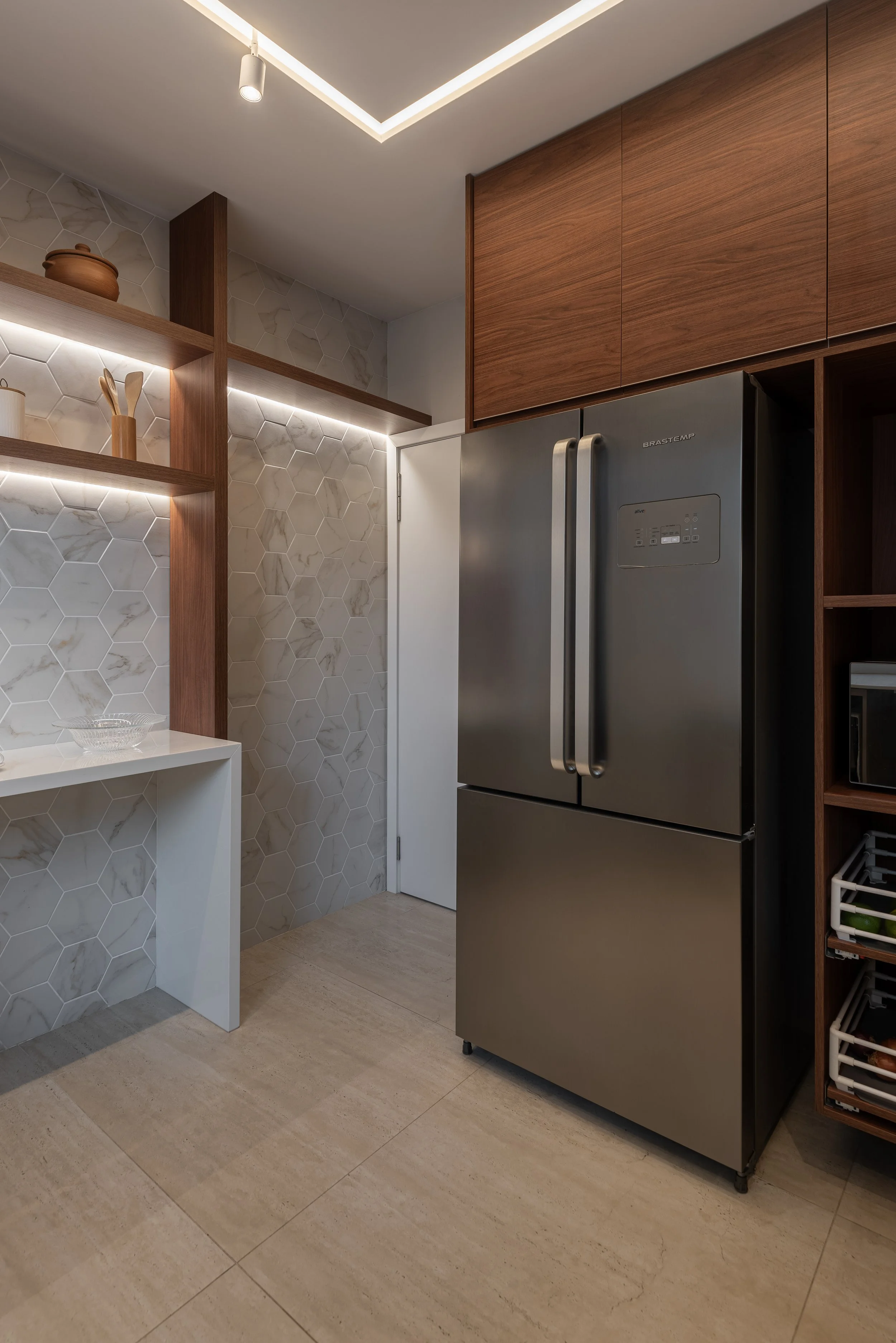 Modern kitchen with a stainless steel double-door refrigerator, wooden upper cabinets, open wooden shelves with kitchen utensils, and a hexagonal marble-patterned backsplash with built-in lighting.