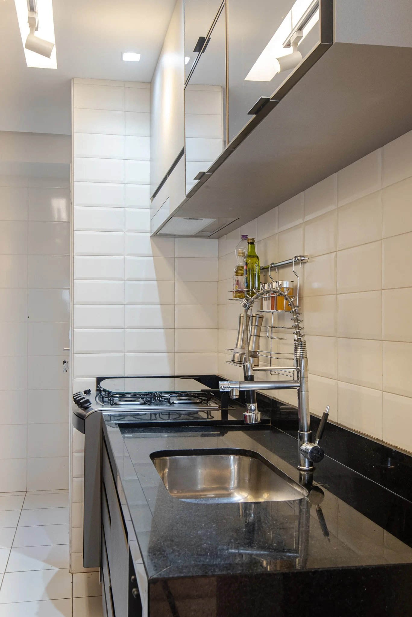 Modern kitchen with black granite countertop, stainless steel sink, and wall-mounted spice rack with bottles and jars.