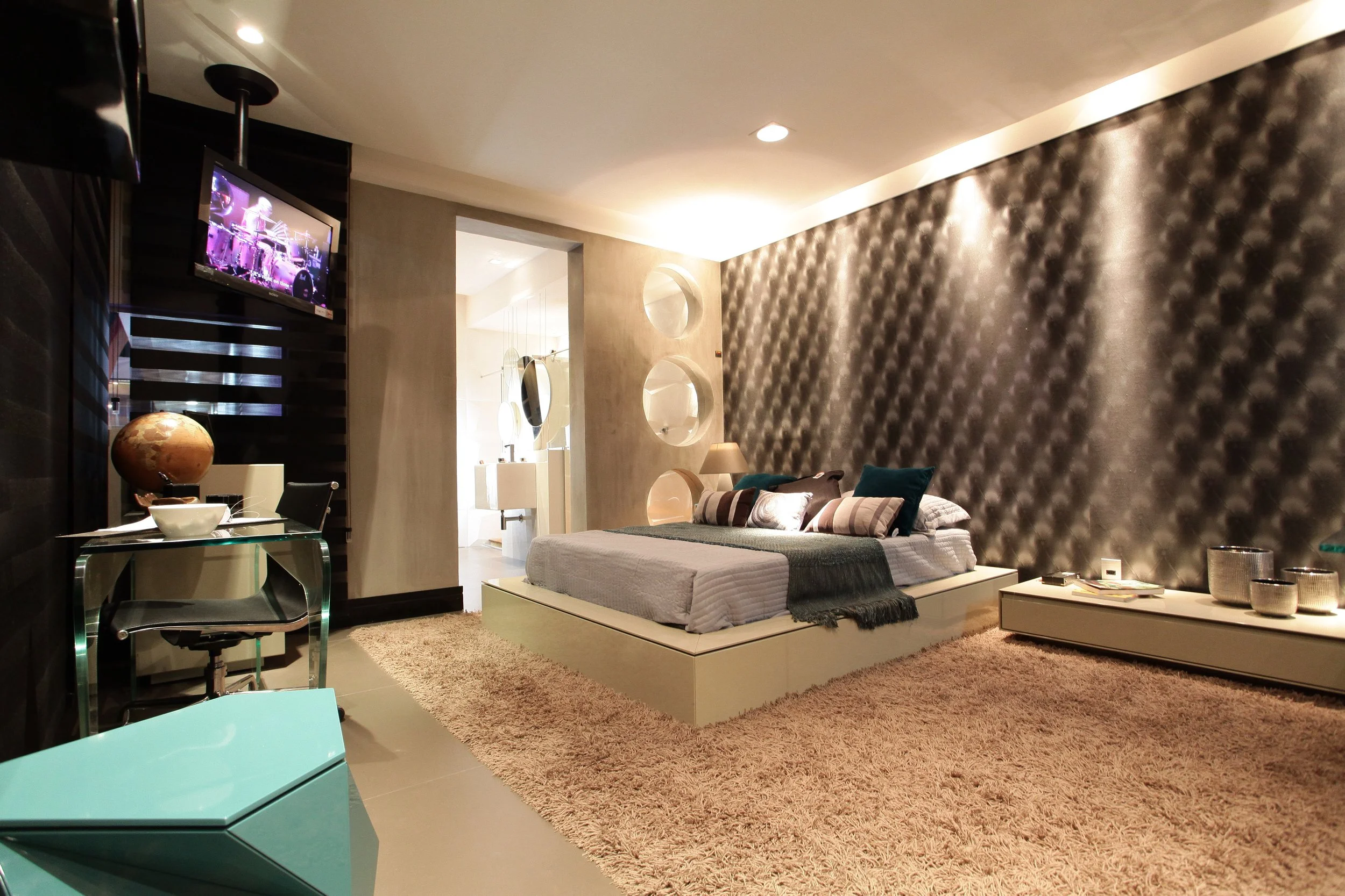 Modern bedroom with a bed, decorative pillows, textured wall, rug, and a TV on the wall.